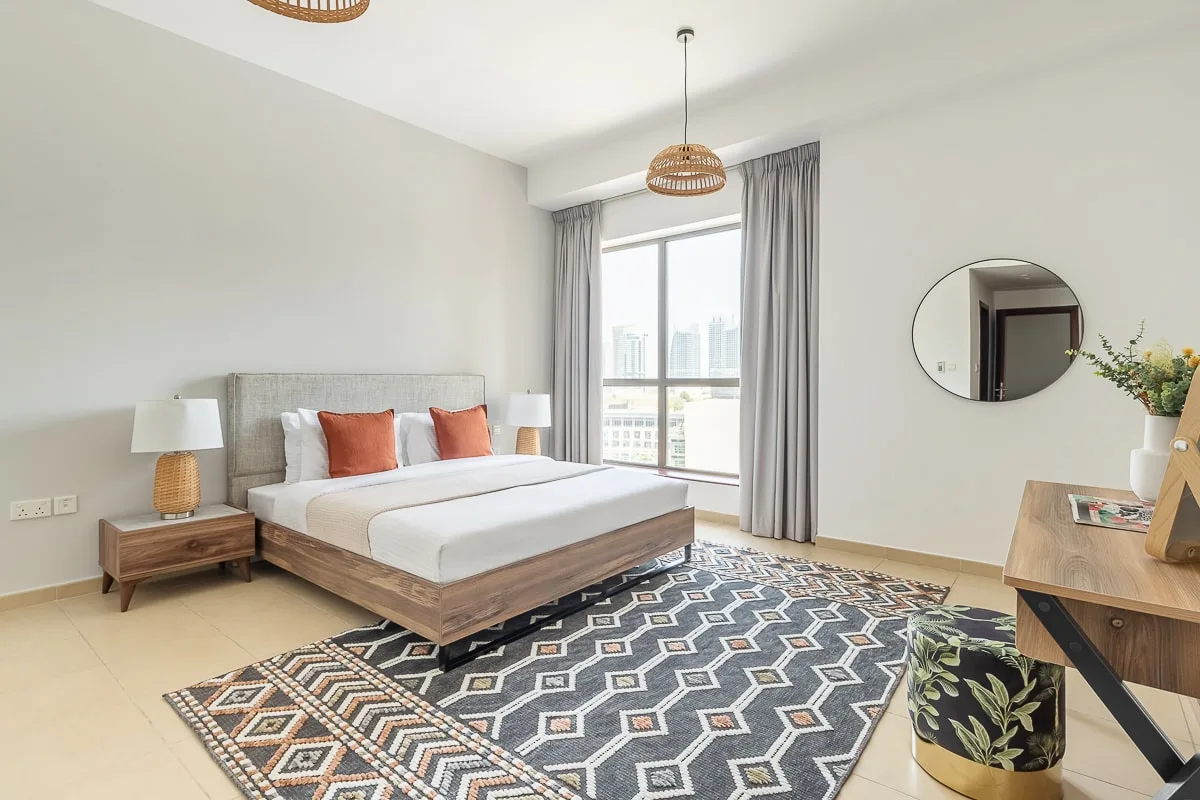 A bright bedroom with a neatly made bed beside a large window.
