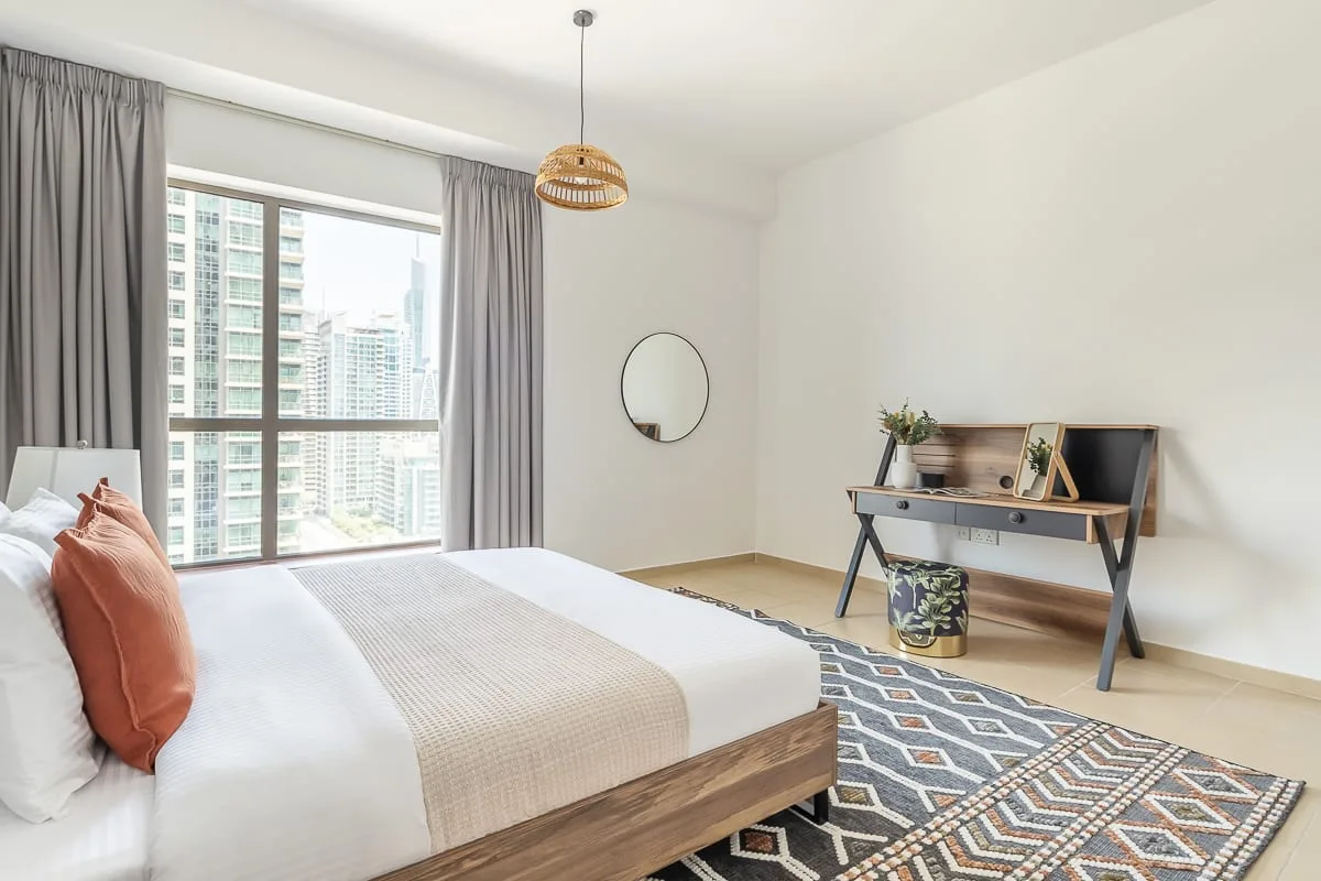 A bright bedroom with a bed, gray curtains, and a patterned rug.