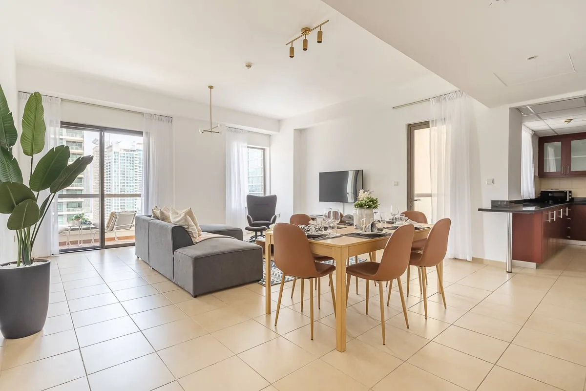 A bright living and dining area with seating, a dining table, and large windows.
