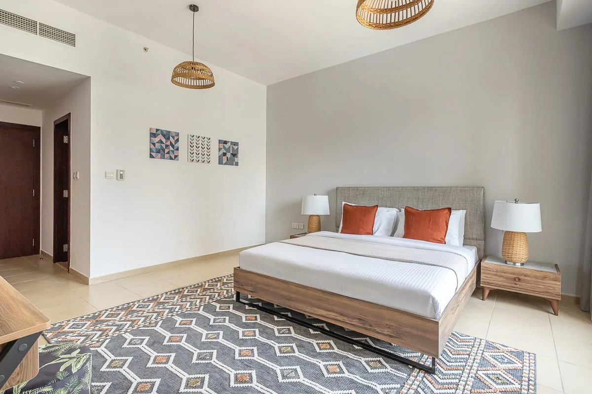 A bedroom with a large bed, bedside tables, and a patterned rug.