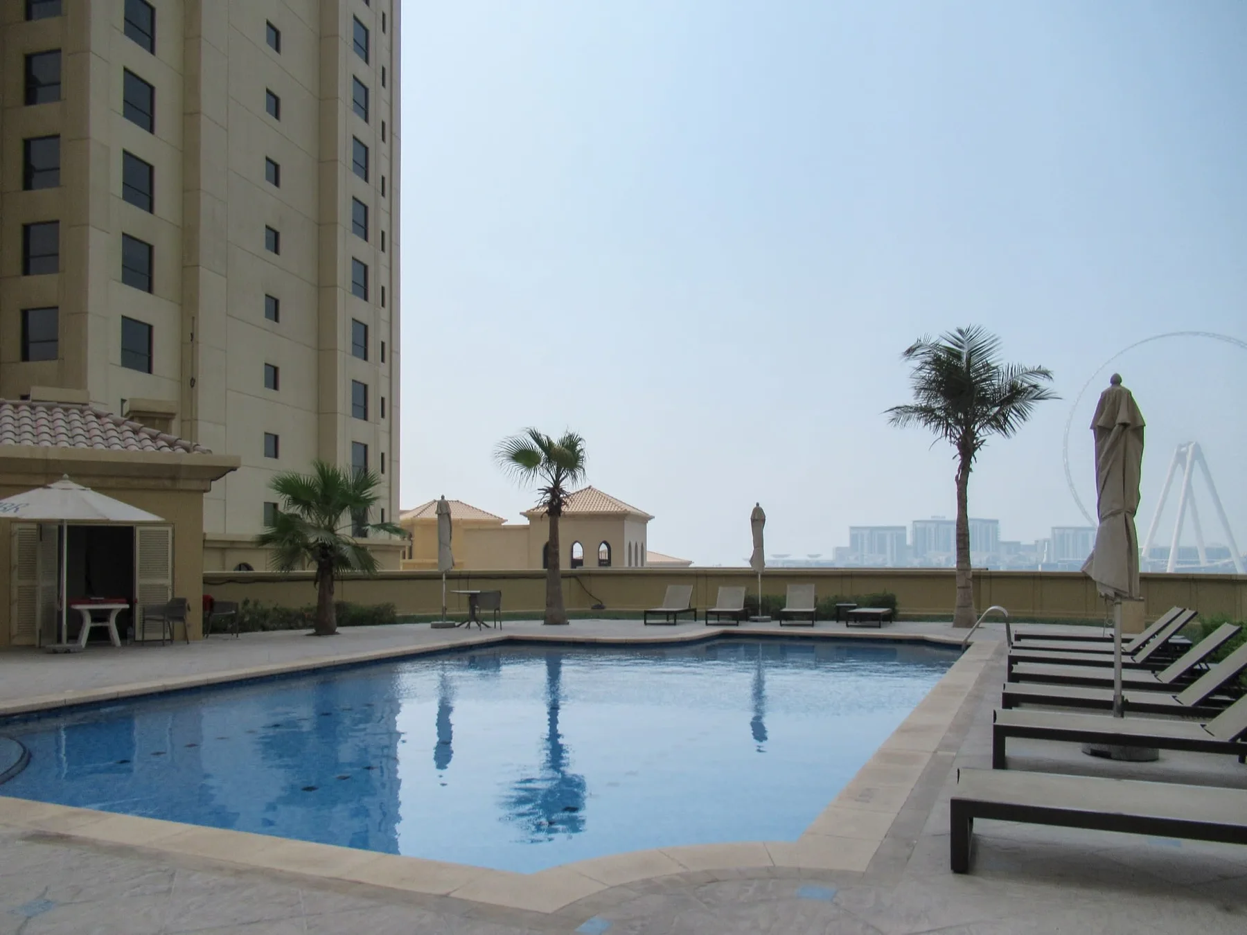 An outdoor swimming pool beside a tall building, with lounge seating along the edge.