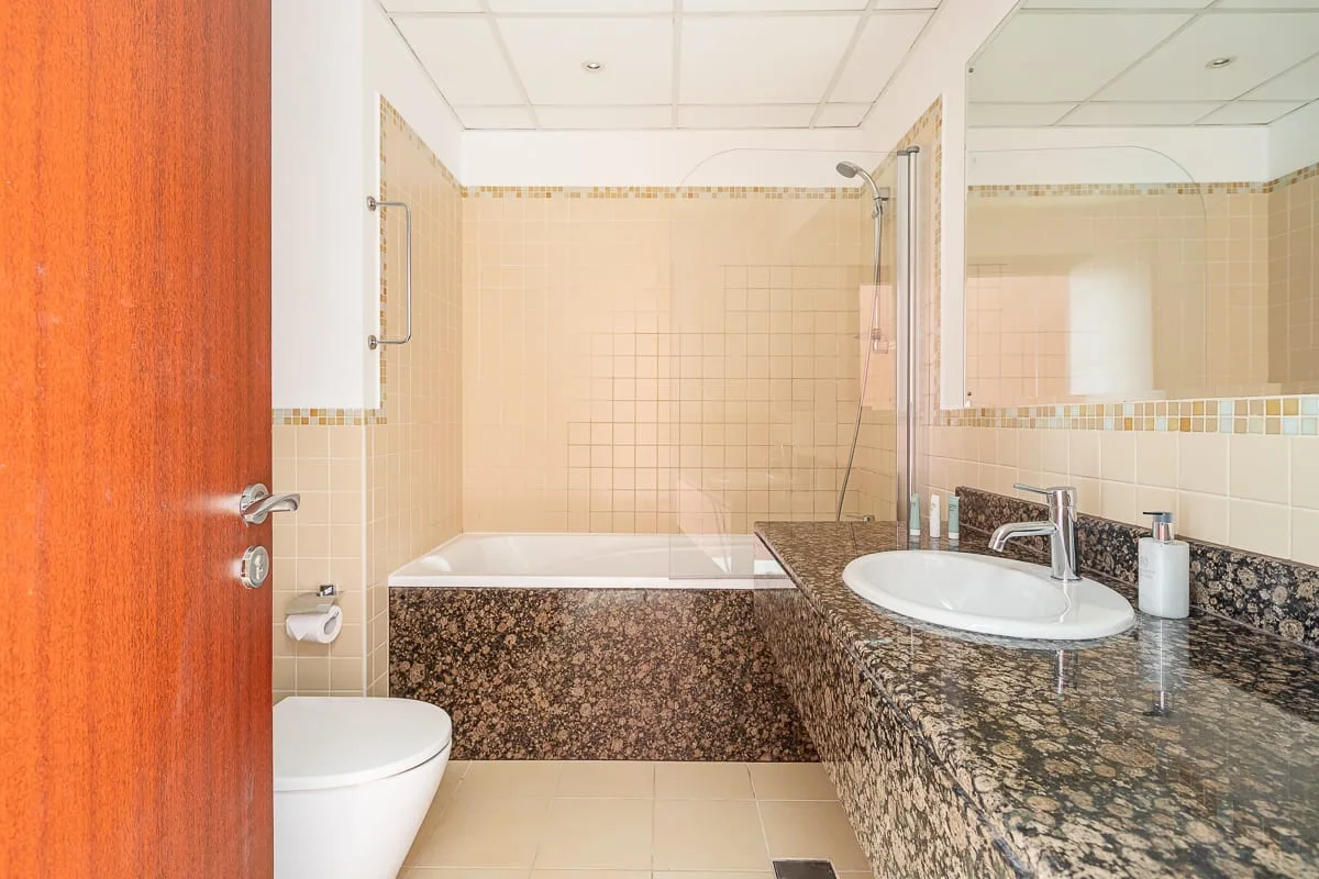 A tiled bathroom with a bathtub, toilet, and sink beside a stone-patterned counter.