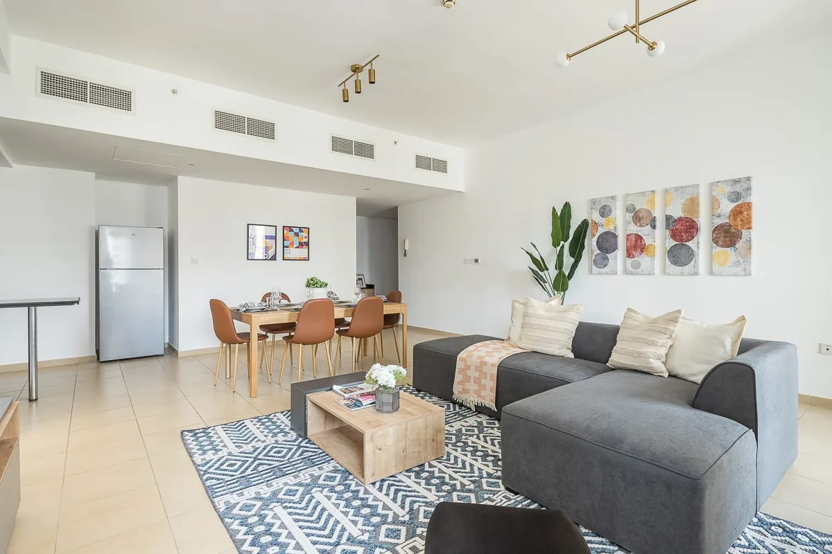 A bright open-plan living and dining area with a gray sectional and wooden table.
