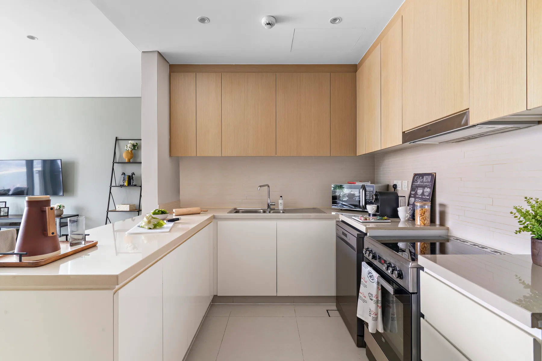 Una cocina moderna con gabinetes de madera clara, encimeras pálidas y electrodomésticos de acero inoxidable.