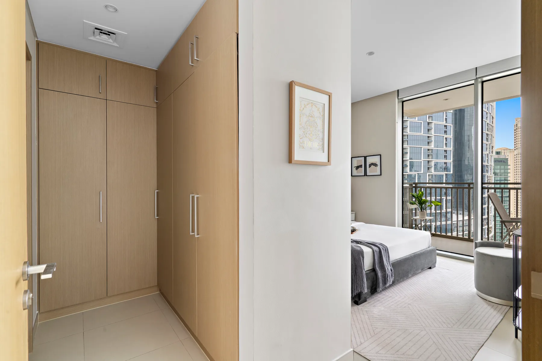 Un dormitorio con una cama junto a ventanales que dan a edificios cercanos.