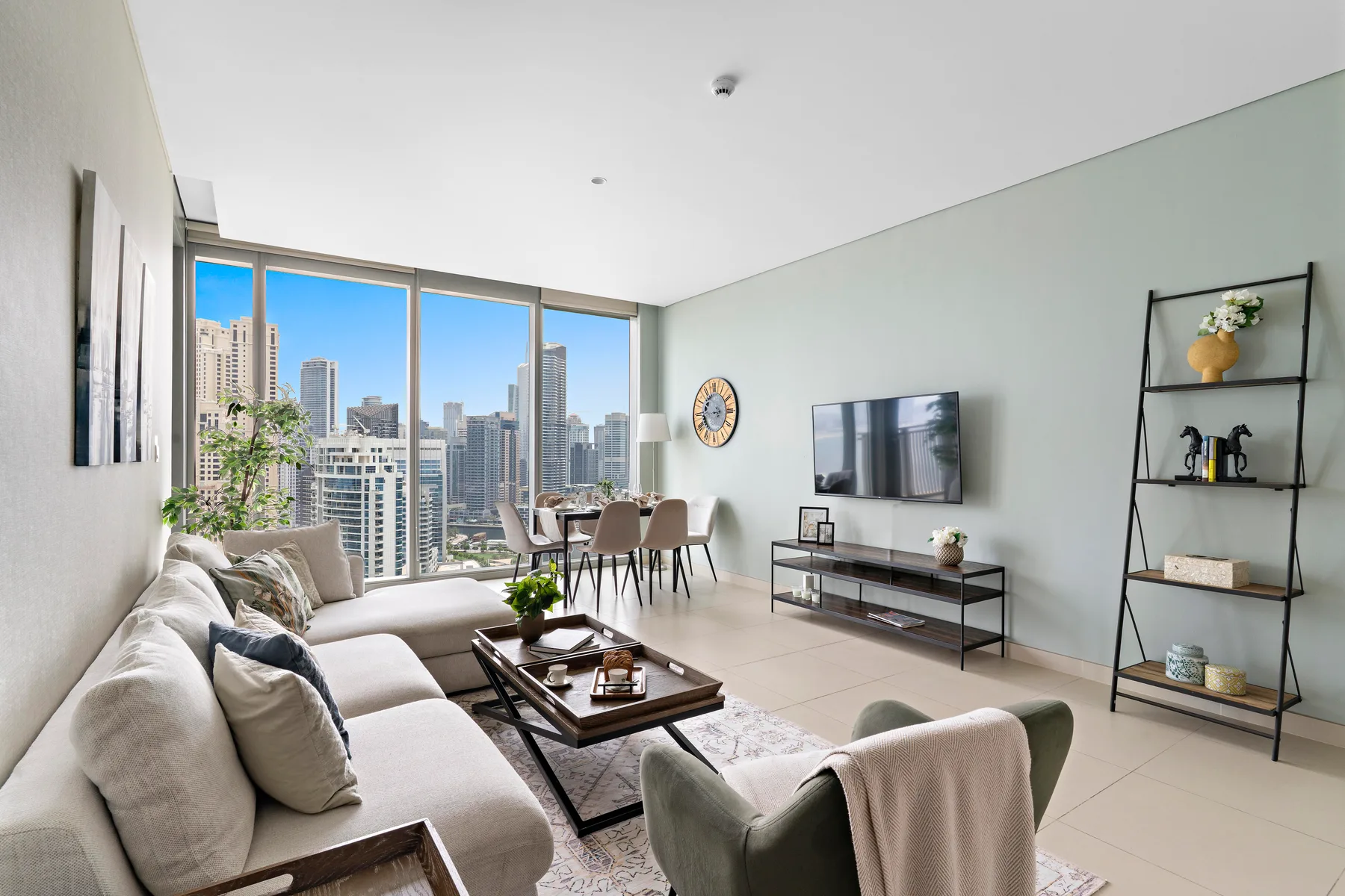 A bright living room with seating, a coffee table, and large city-facing windows.