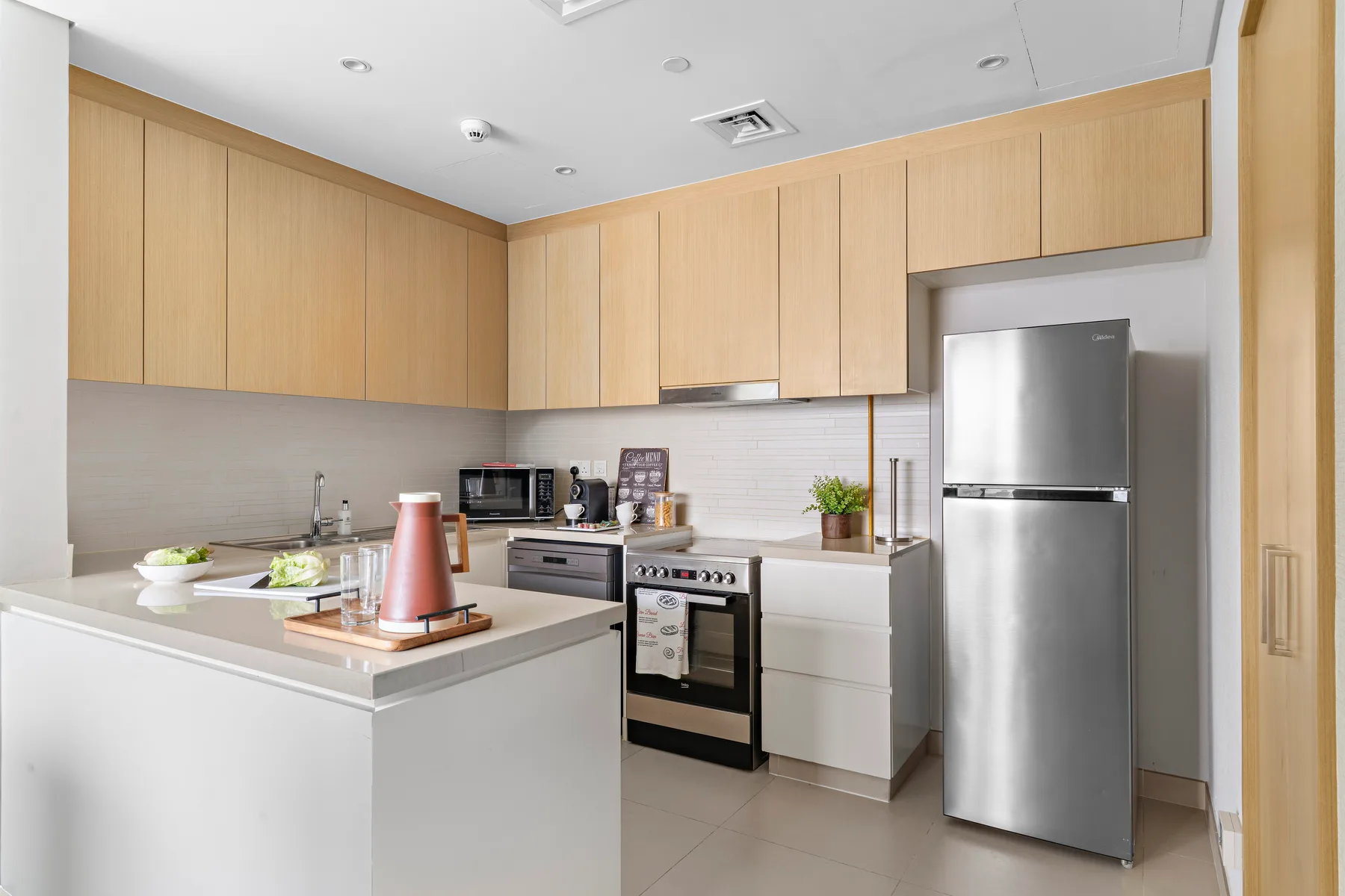 Una cocina moderna con gabinetes de madera clara, una isla blanca y electrodomésticos de acero inoxidable.