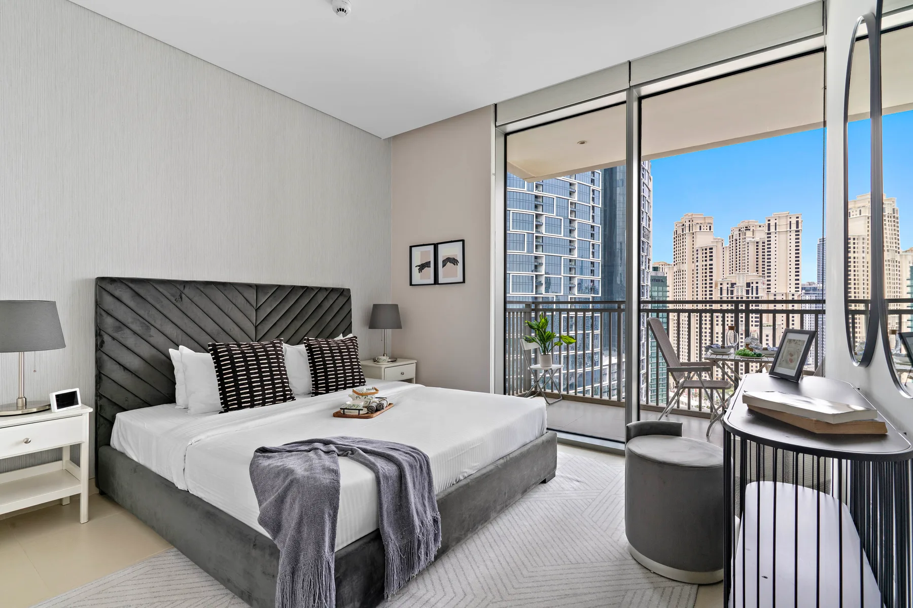 Un dormitorio con una cama tendida junto a ventanas de piso a techo con vistas a edificios de la ciudad.