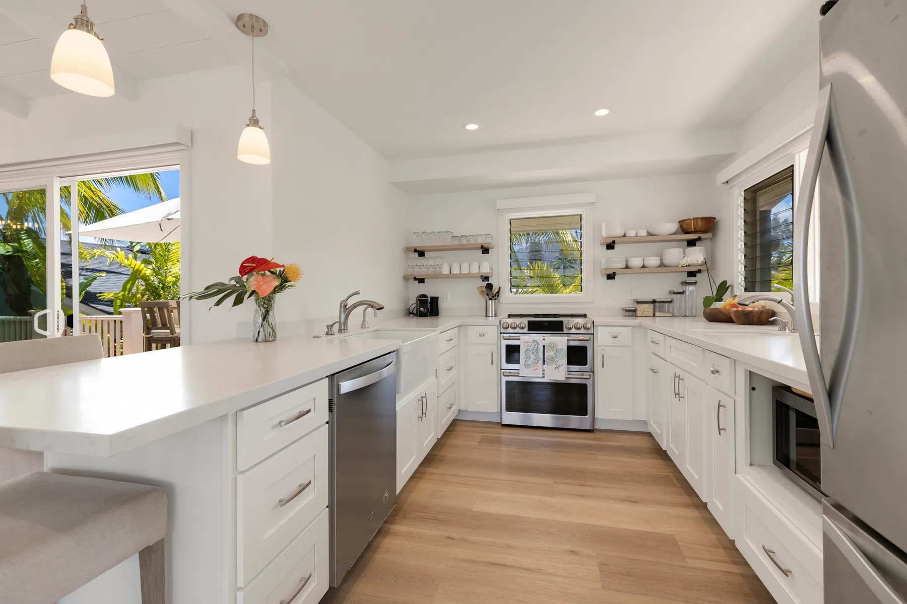 Una cocina blanca y luminosa con una isla, electrodomésticos de acero inoxidable y ventanas.