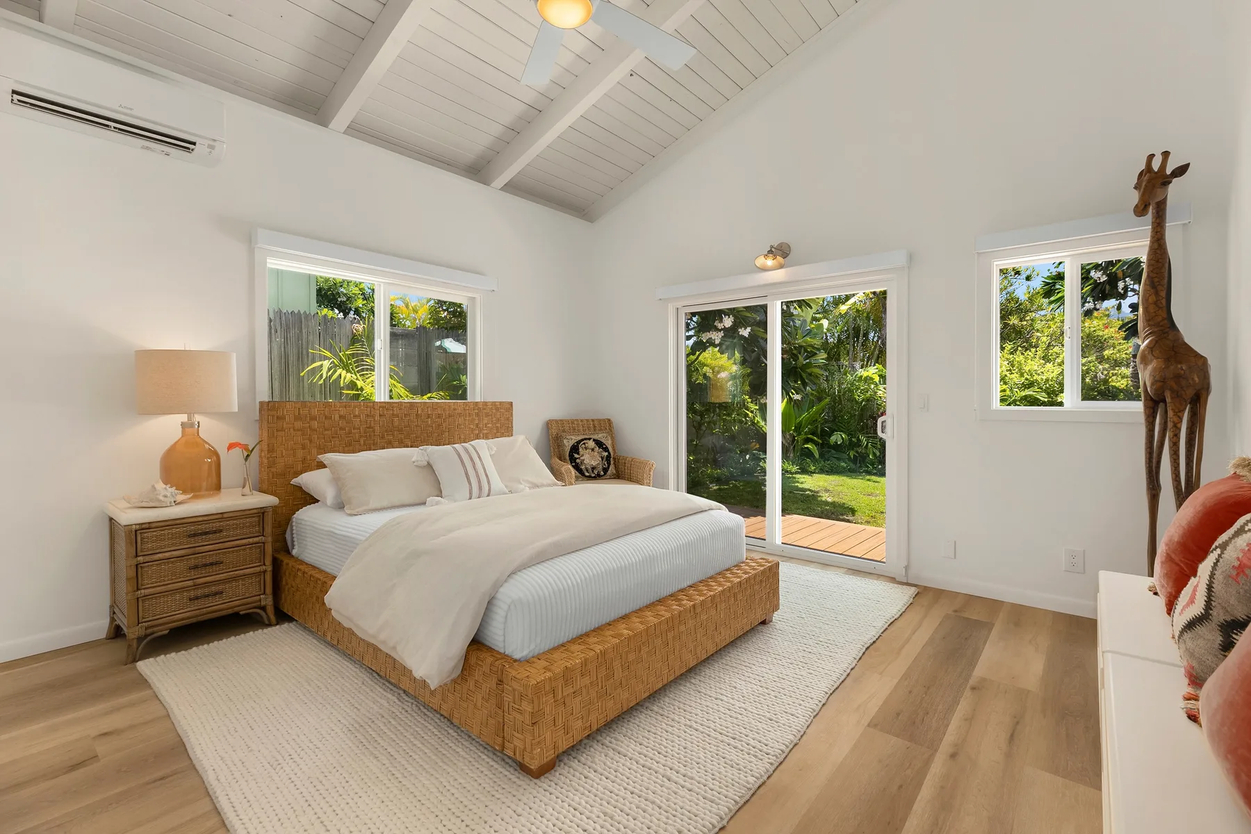 Un dormitorio luminoso con una cama, una mesita de noche y ventanas con vistas a la vegetación.