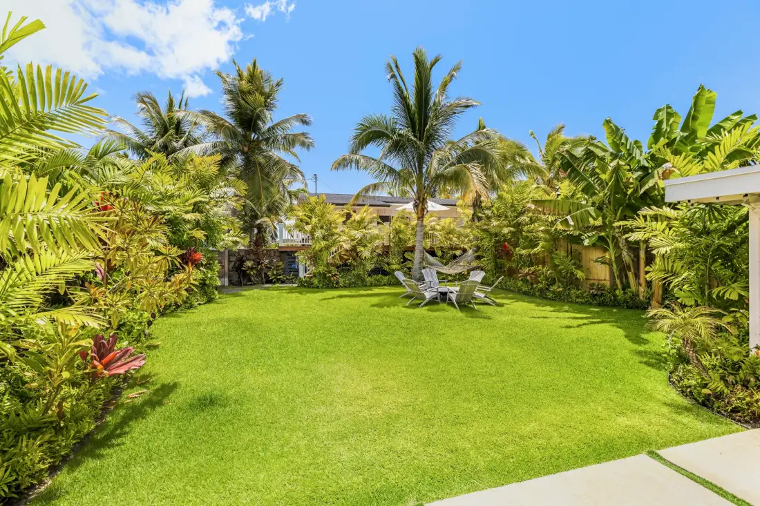 Un jardín tropical con césped amplio, palmeras y asientos al aire libre.