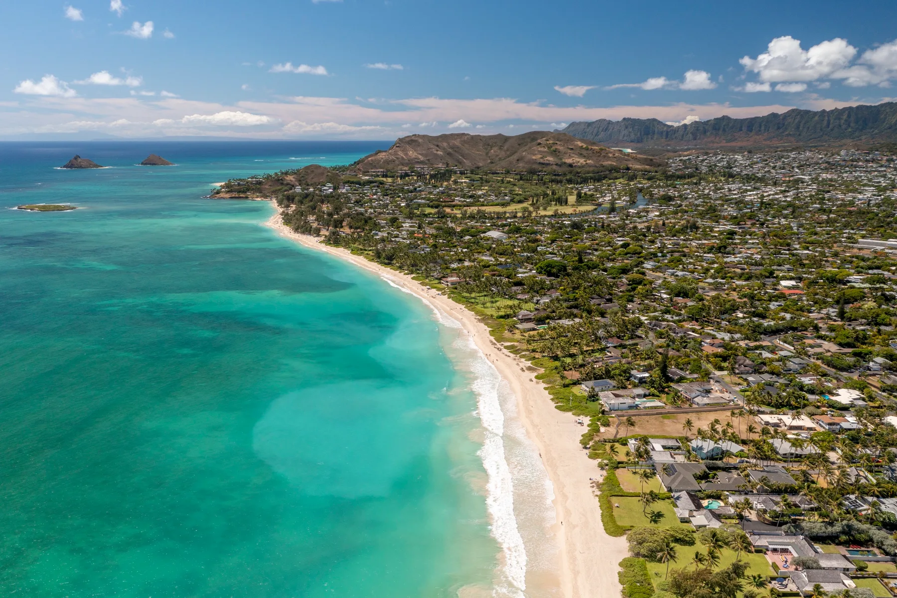 Vista aérea de una larga playa de arena junto a aguas turquesas y una costa urbanizada.