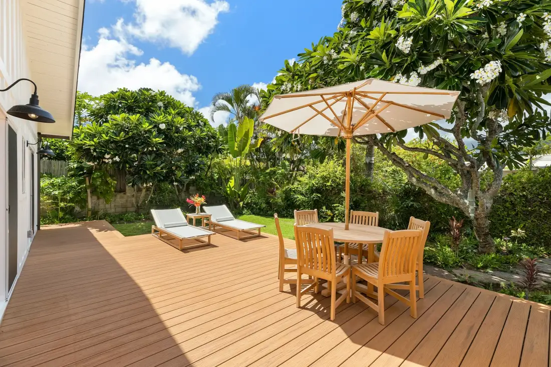 Una zona de comedor en una terraza de madera con mesa y sombrilla, rodeada de vegetación.