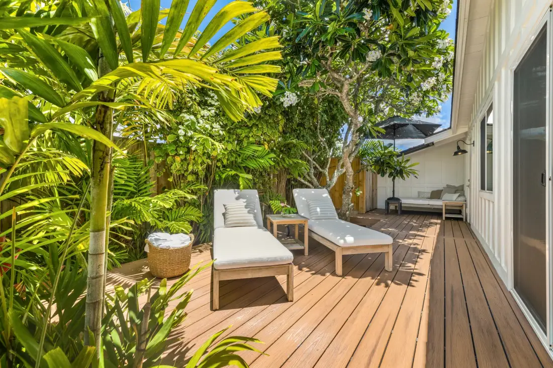Una terraza de madera con asientos de descanso está rodeada de abundantes plantas tropicales.