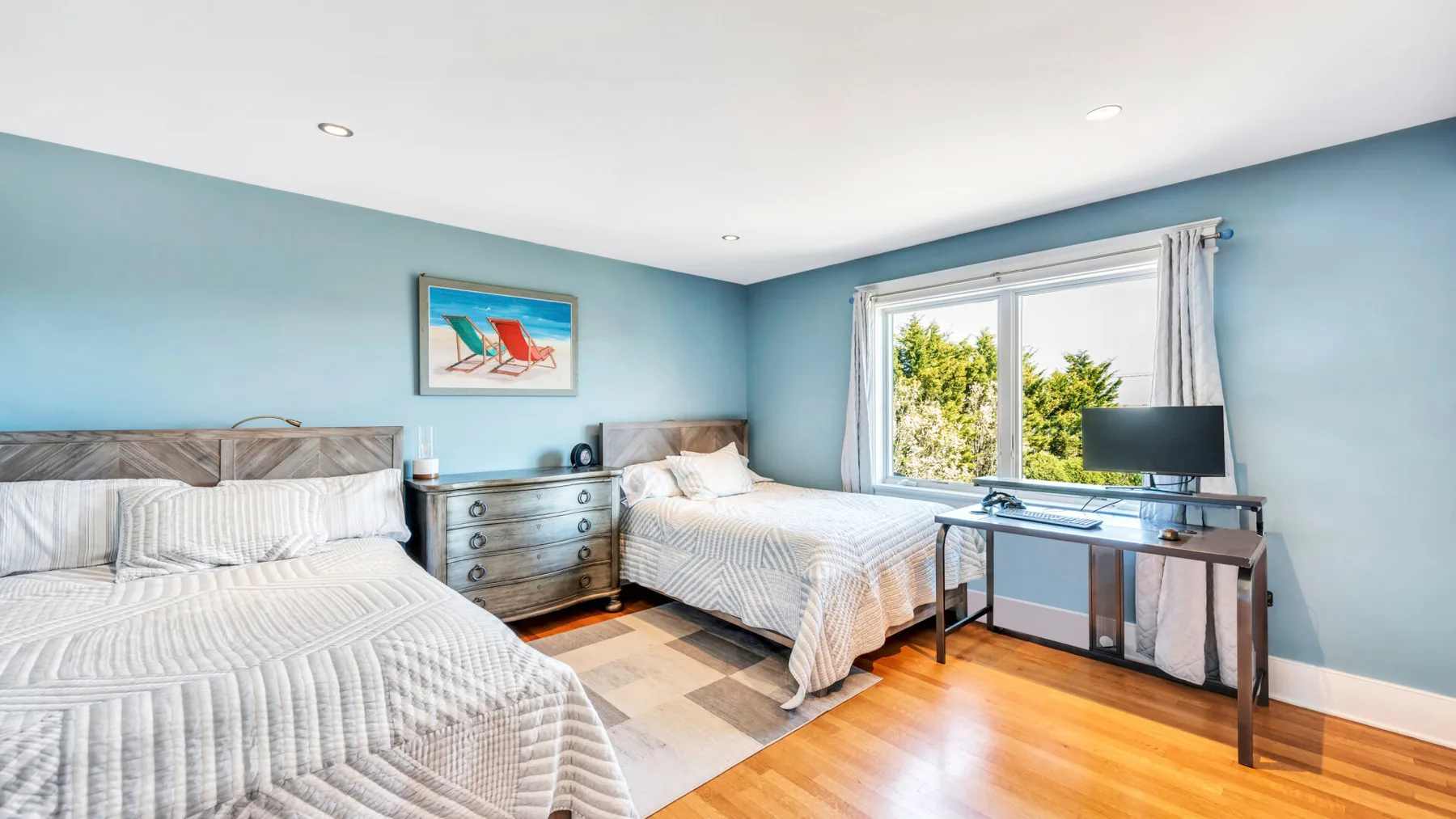 Un dormitorio con dos camas, una cómoda y un escritorio junto a una ventana grande.