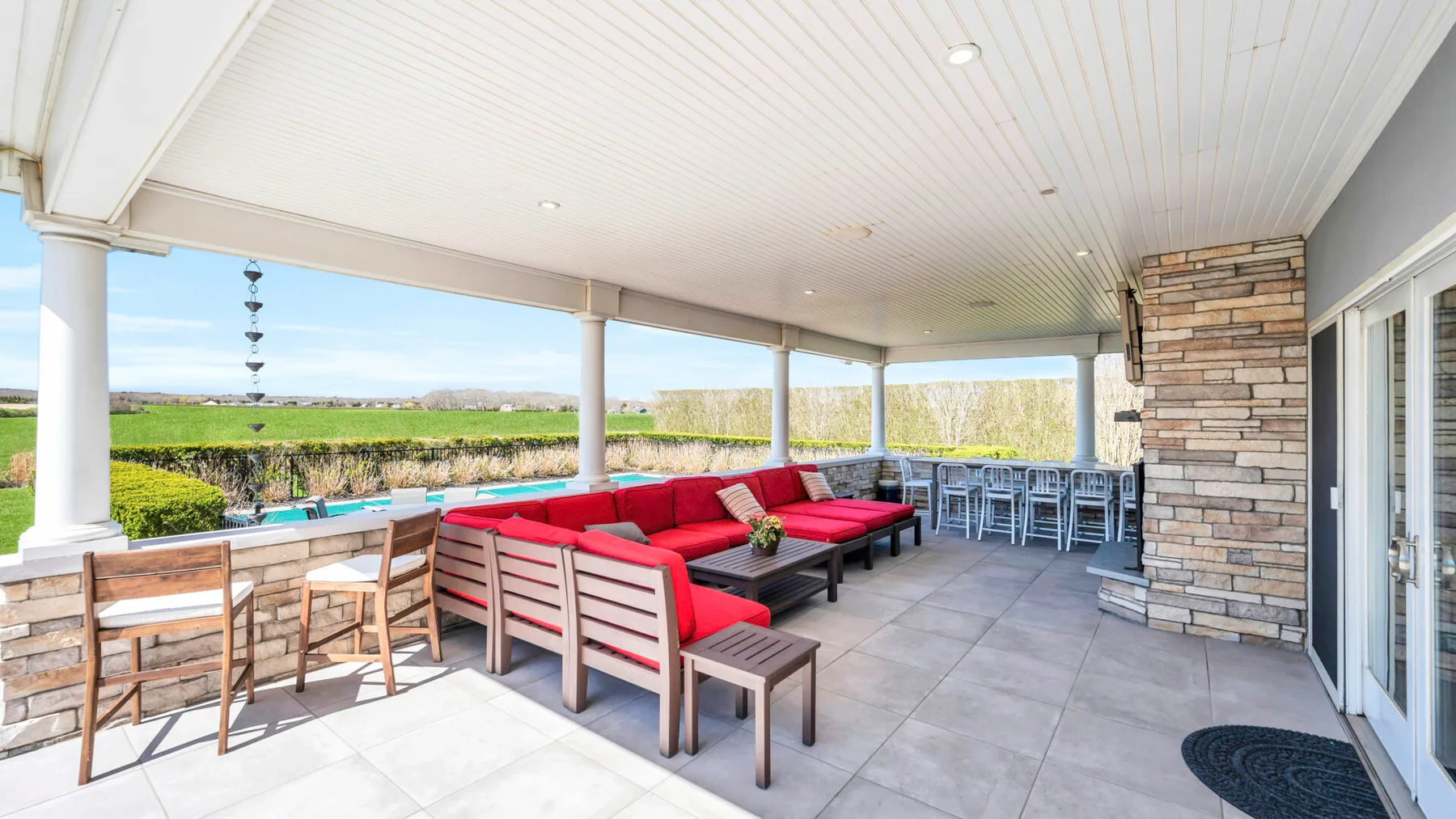 Un patio cubierto tiene asientos rojos, una mesa de comedor y vistas abiertas a los campos.