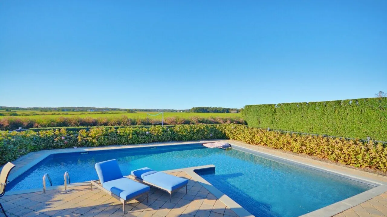 Una piscina exterior está rodeada por una terraza pavimentada y asientos reclinables.
