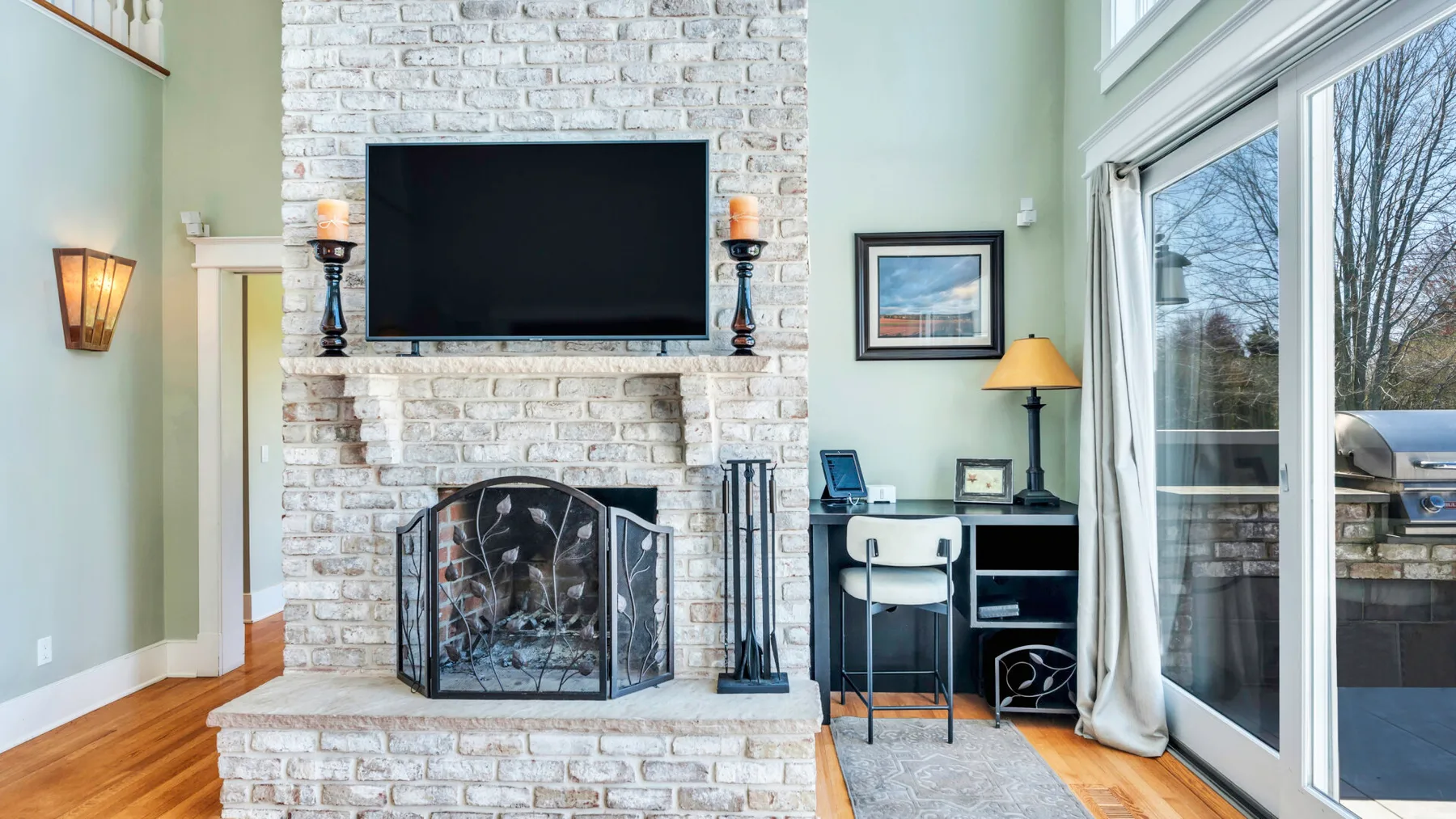 Una sala luminosa con chimenea de ladrillo, televisor y grandes puertas de vidrio.
