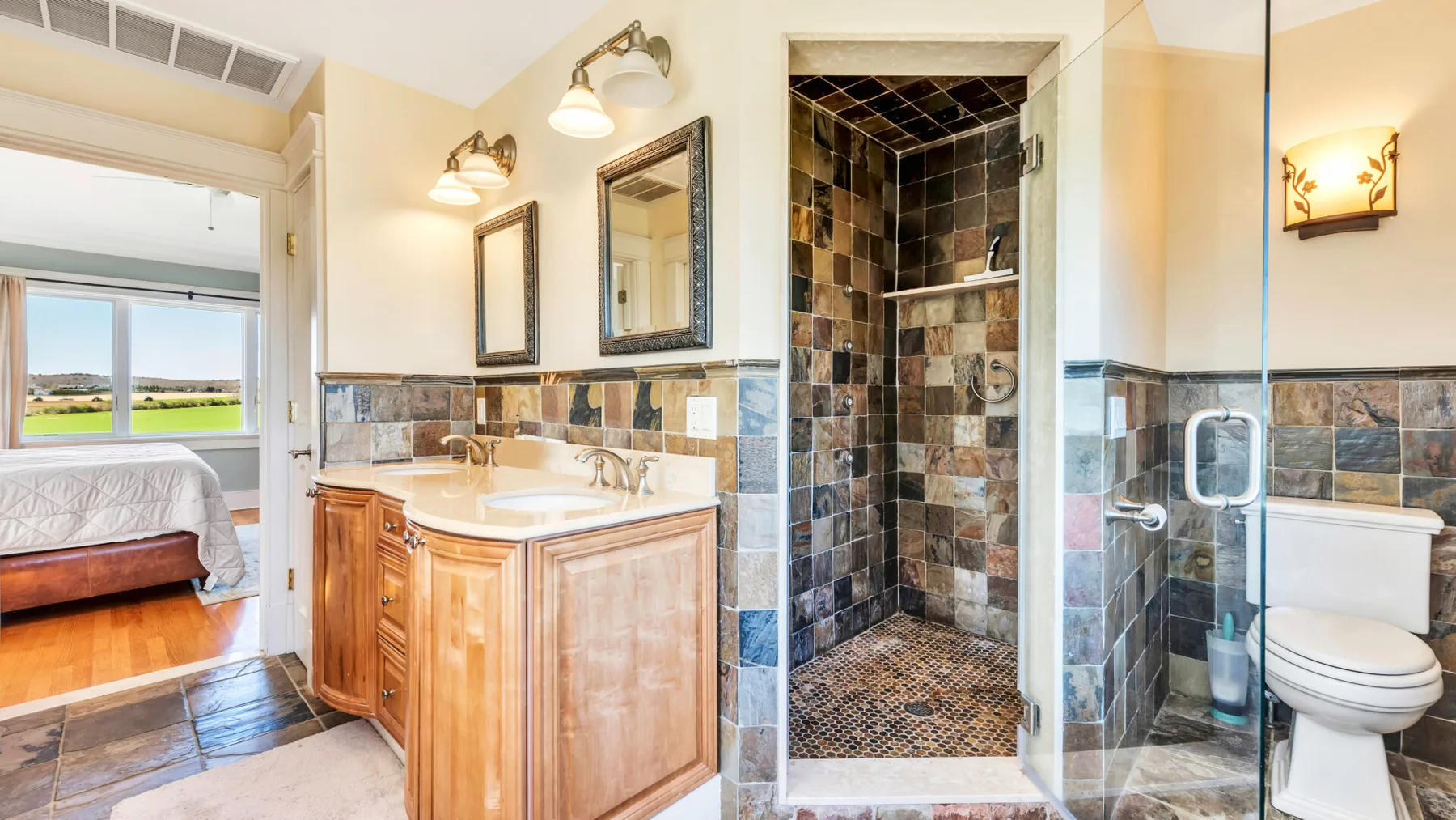 Un baño con un tocador de madera, una ducha con azulejos y una puerta a un dormitorio.
