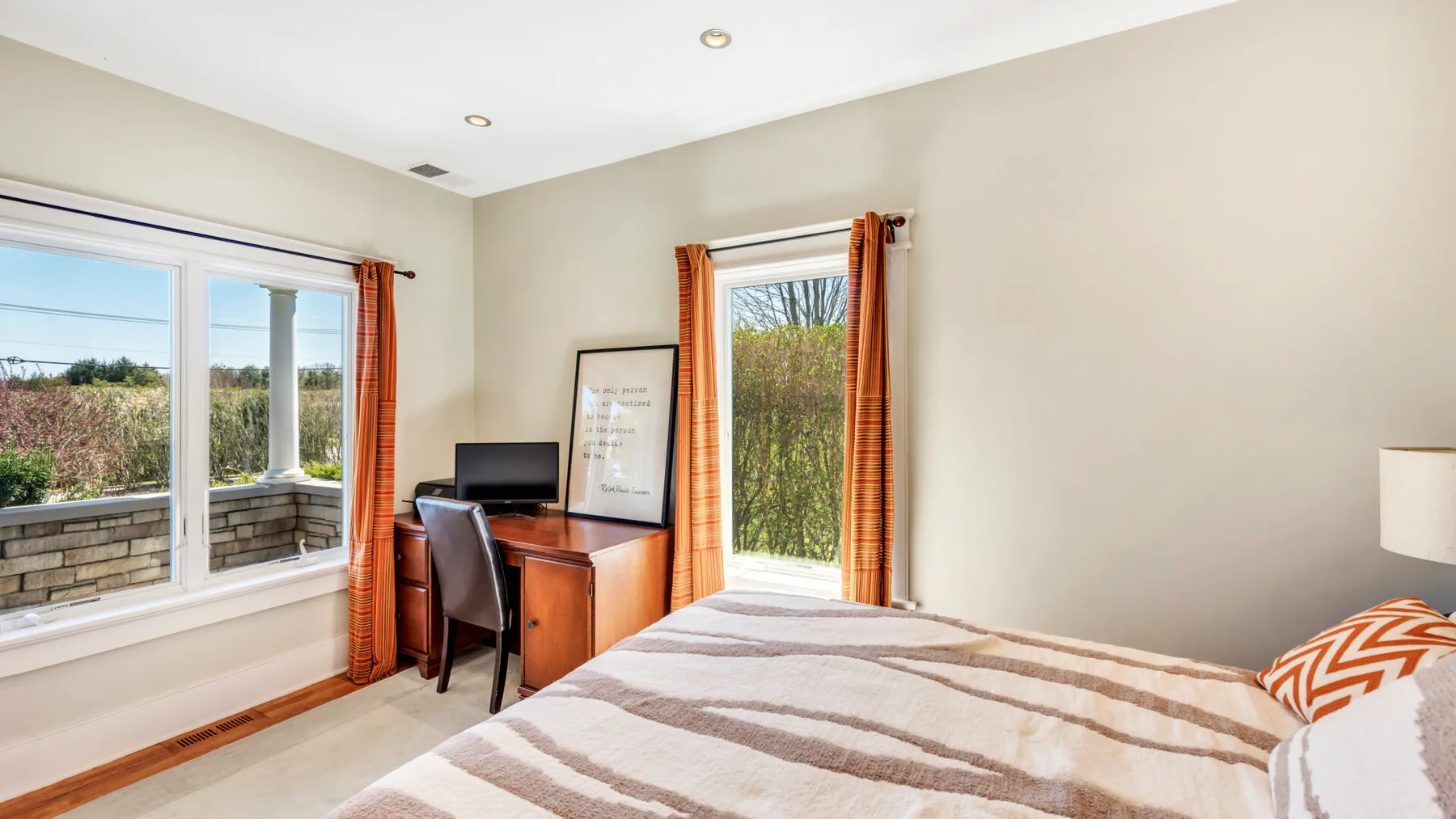Un dormitorio luminoso con cama, escritorio y ventanas con vistas a la vegetación.