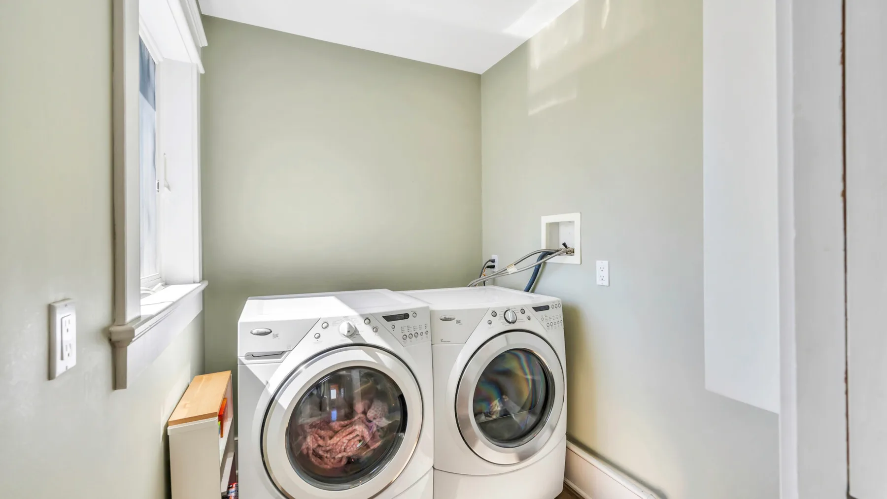 Un cuarto de lavandería con lavadora y secadora de carga frontal junto a una ventana.