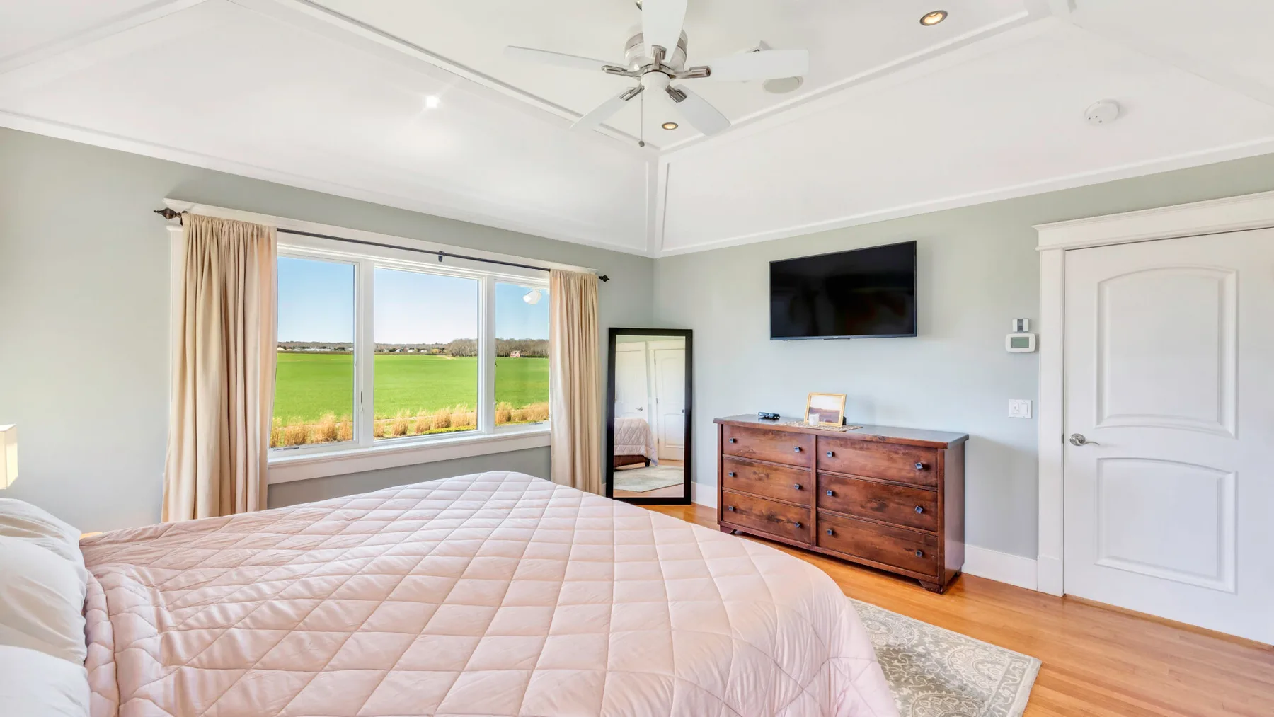Un dormitorio luminoso con una cama grande, una ventana y una cómoda de madera.