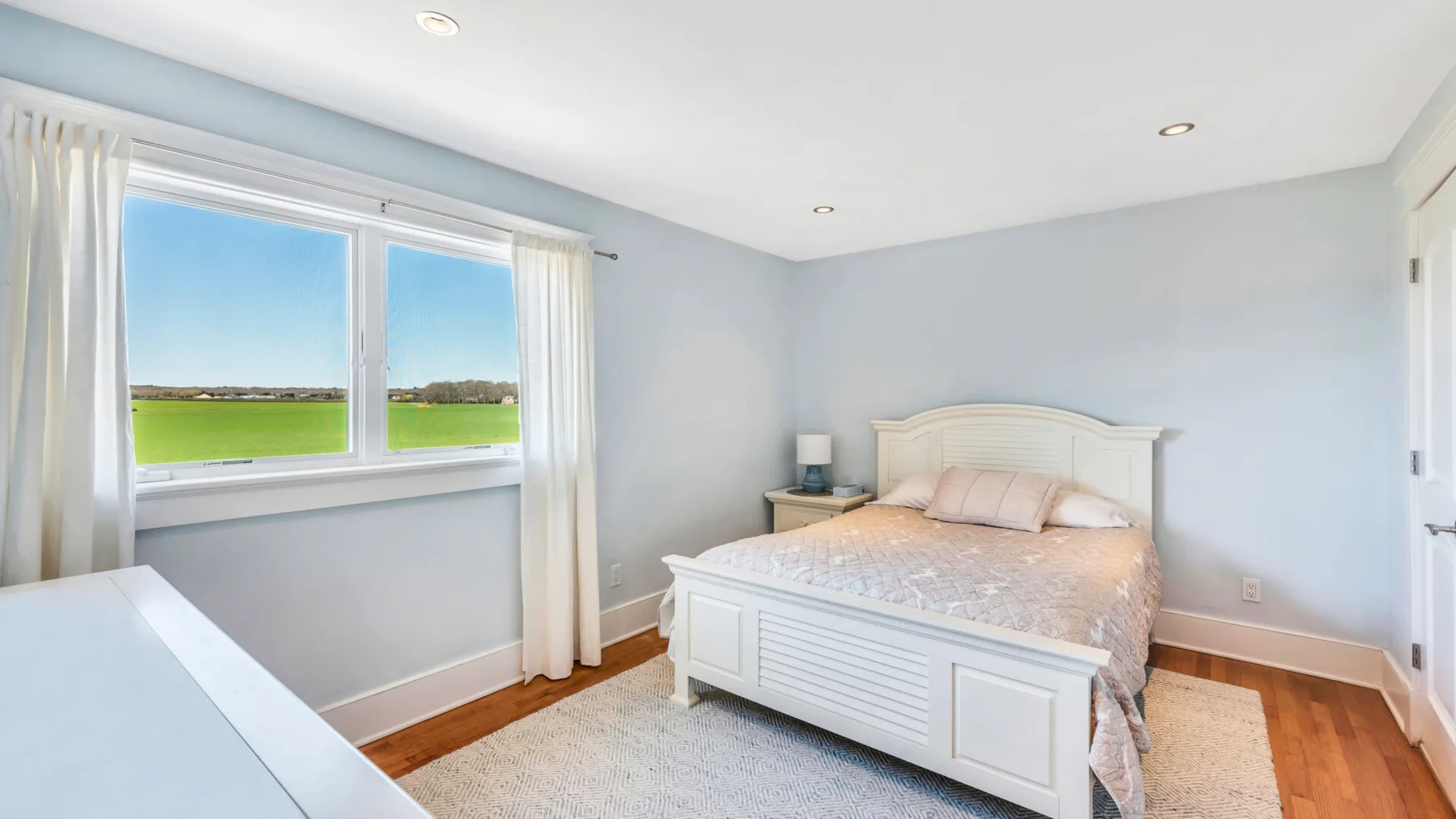 Un dormitorio con una cama junto a una ventana amplia con vistas a campos verdes.