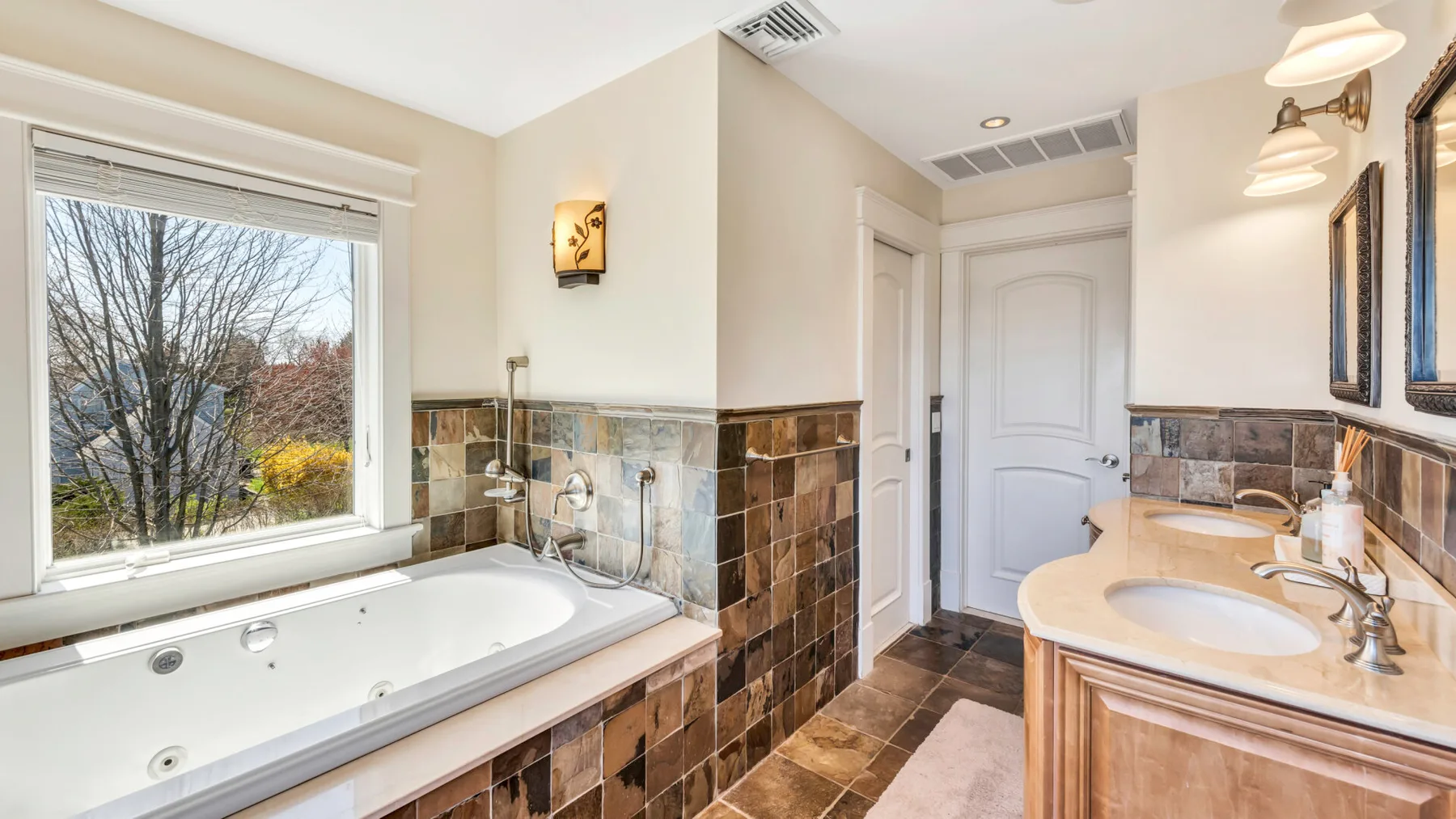 Un baño con bañera, lavabo y una ventana con vistas a los árboles.