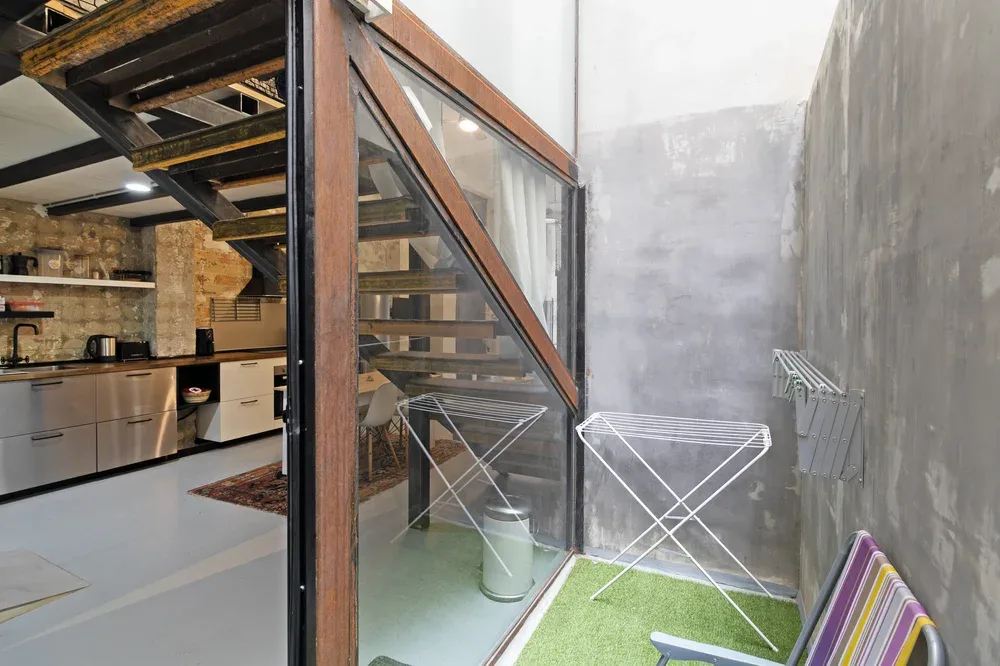 Un pequeño patio junto a una cocina, con tendederos y una pared de vidrio.