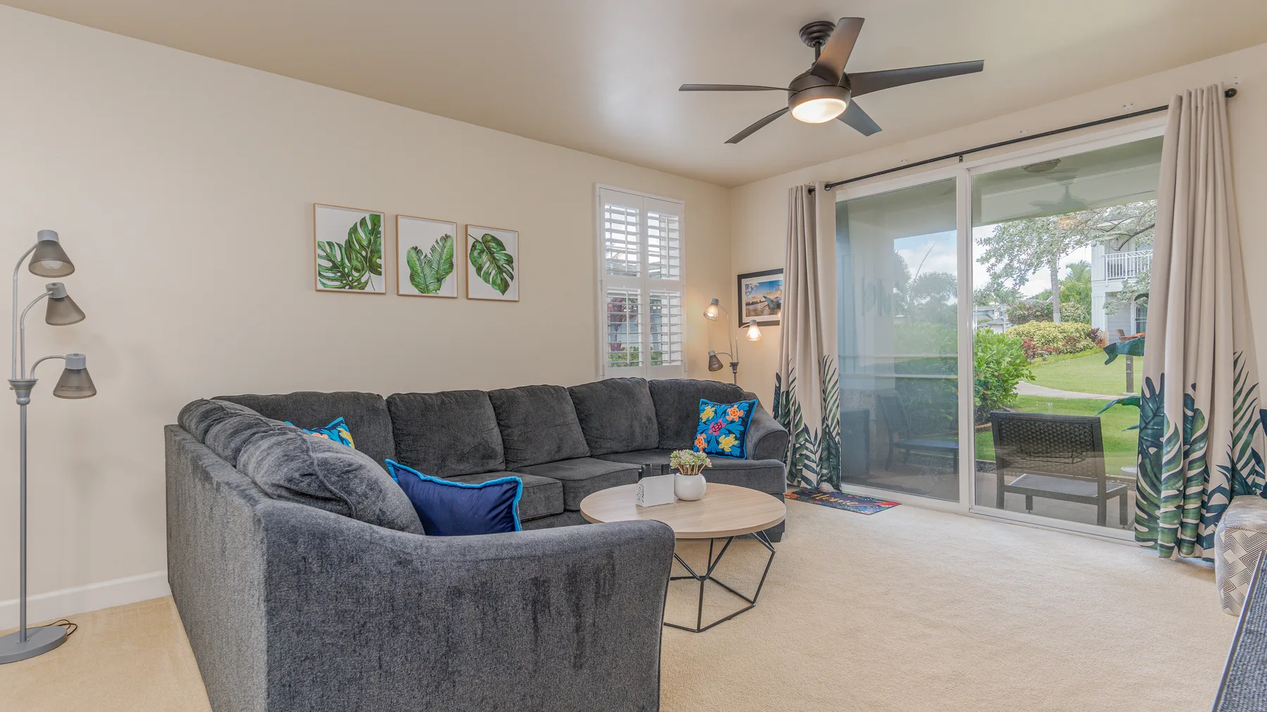 A living room with gray seating, a coffee table, and sliding glass doors opening to a patio.