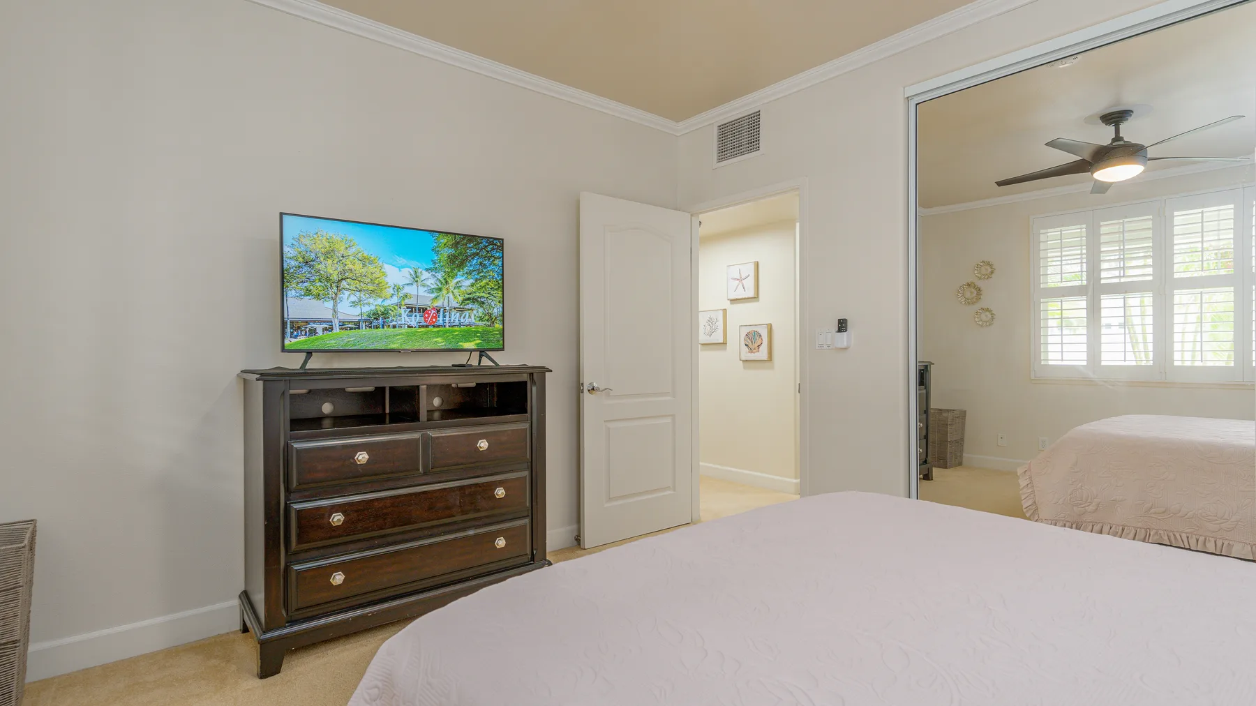 A bedroom with a television on a dresser and an open doorway to another sleeping area.