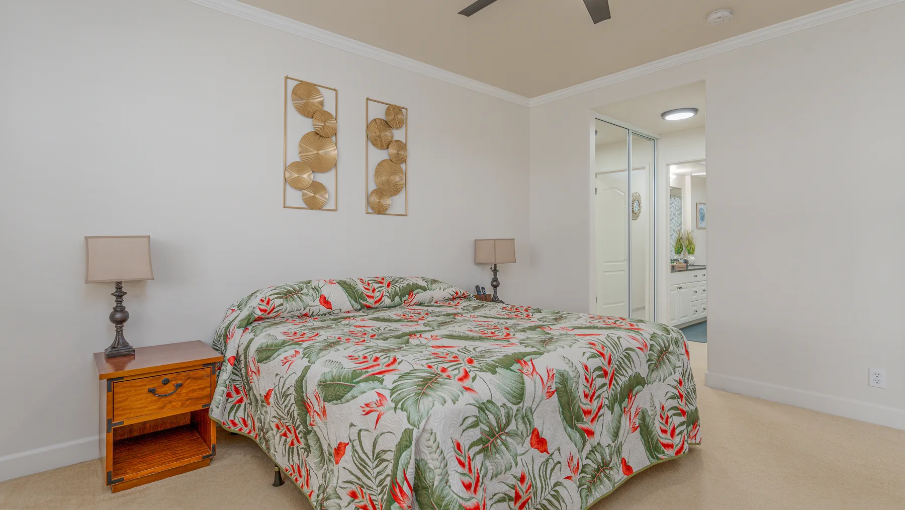 A bedroom with a bed covered in a leafy floral-patterned bedspread.