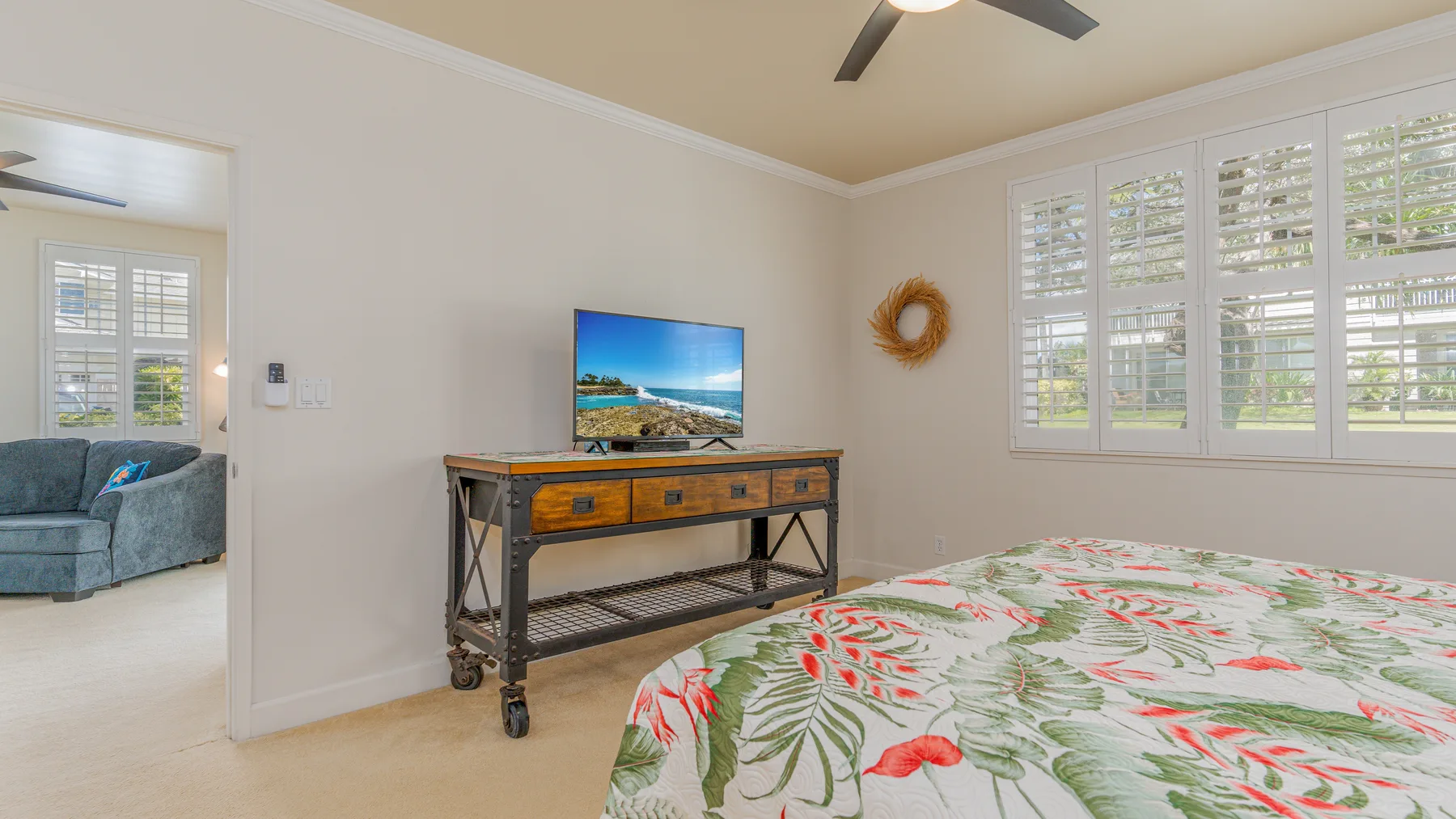 A bedroom with a floral bedspread, a television, and windows with shutters.