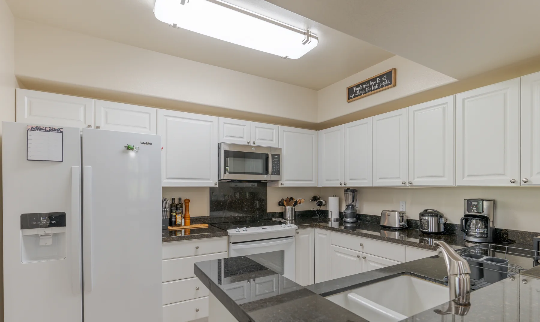 A bright kitchen with white cabinets, dark countertops, and a central island.