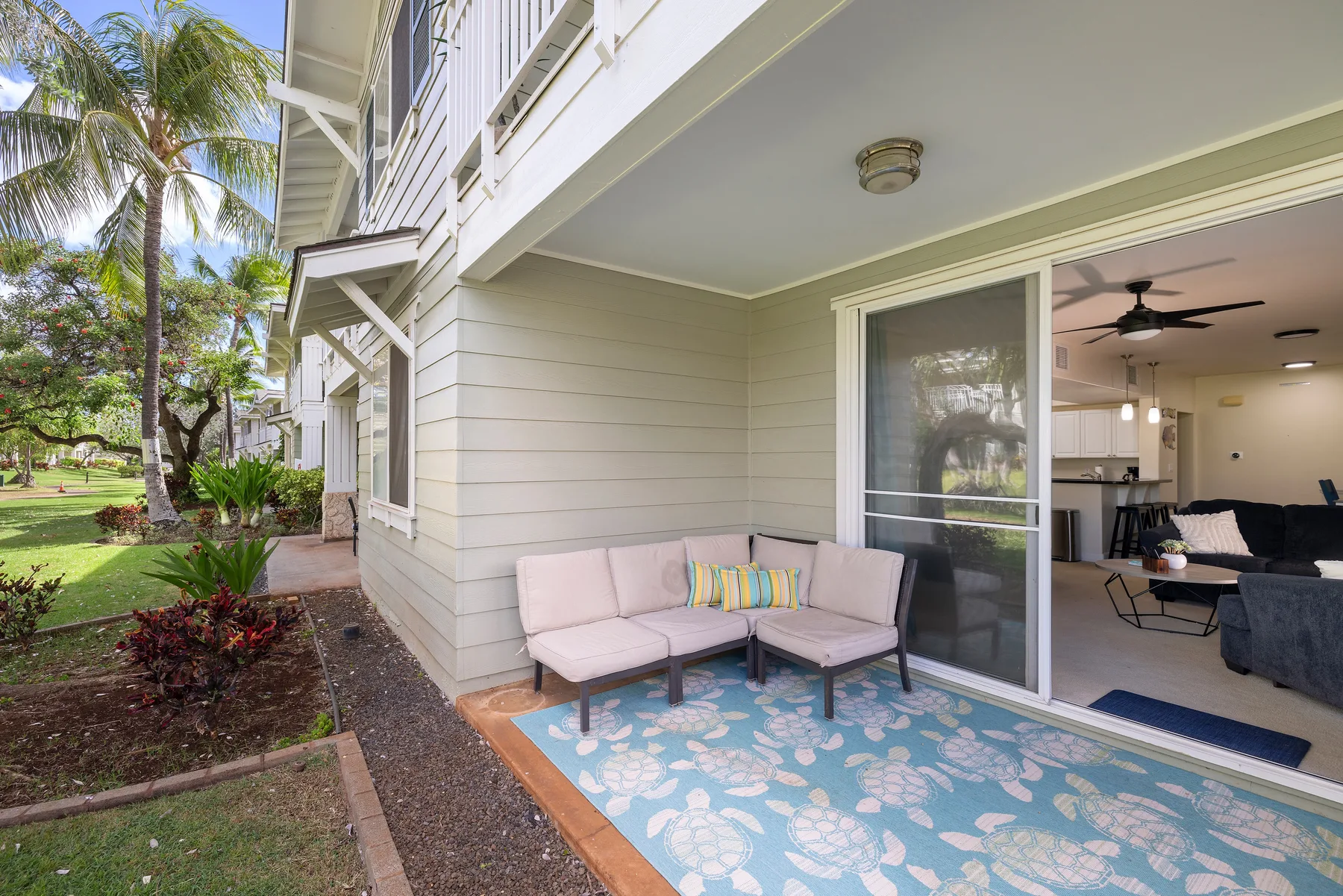 A covered patio with outdoor seating overlooks a landscaped lawn and palm trees.