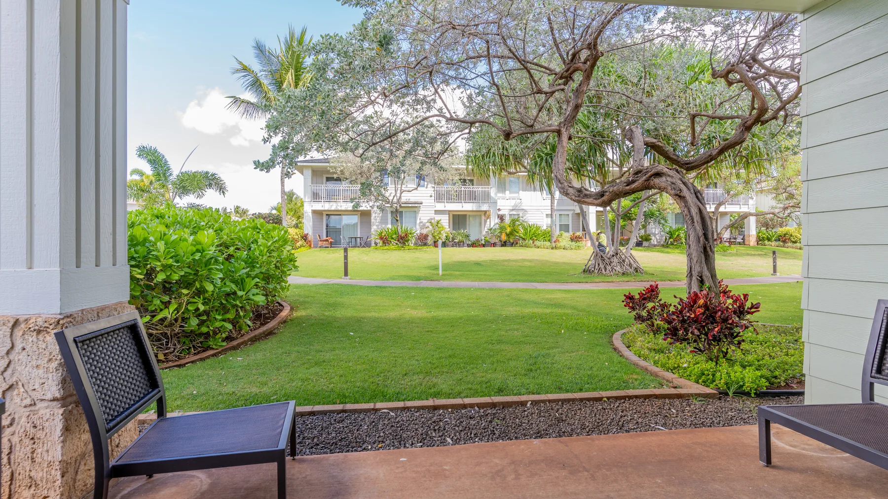 A covered patio overlooks a landscaped courtyard with a lawn and trees.