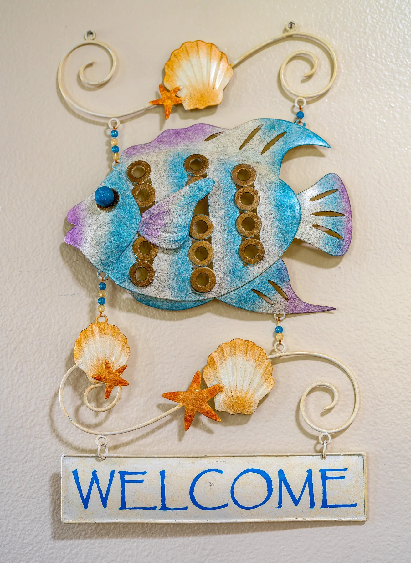 A decorative fish wall hanging with shells and a welcome sign.