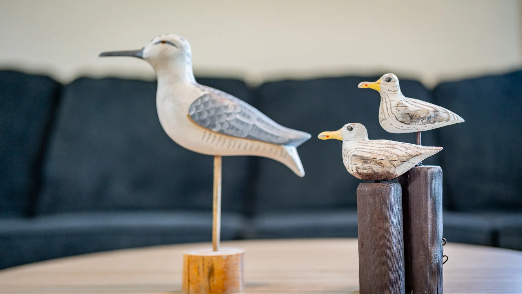 A living room with a dark couch and three decorative wooden bird figures on a table.