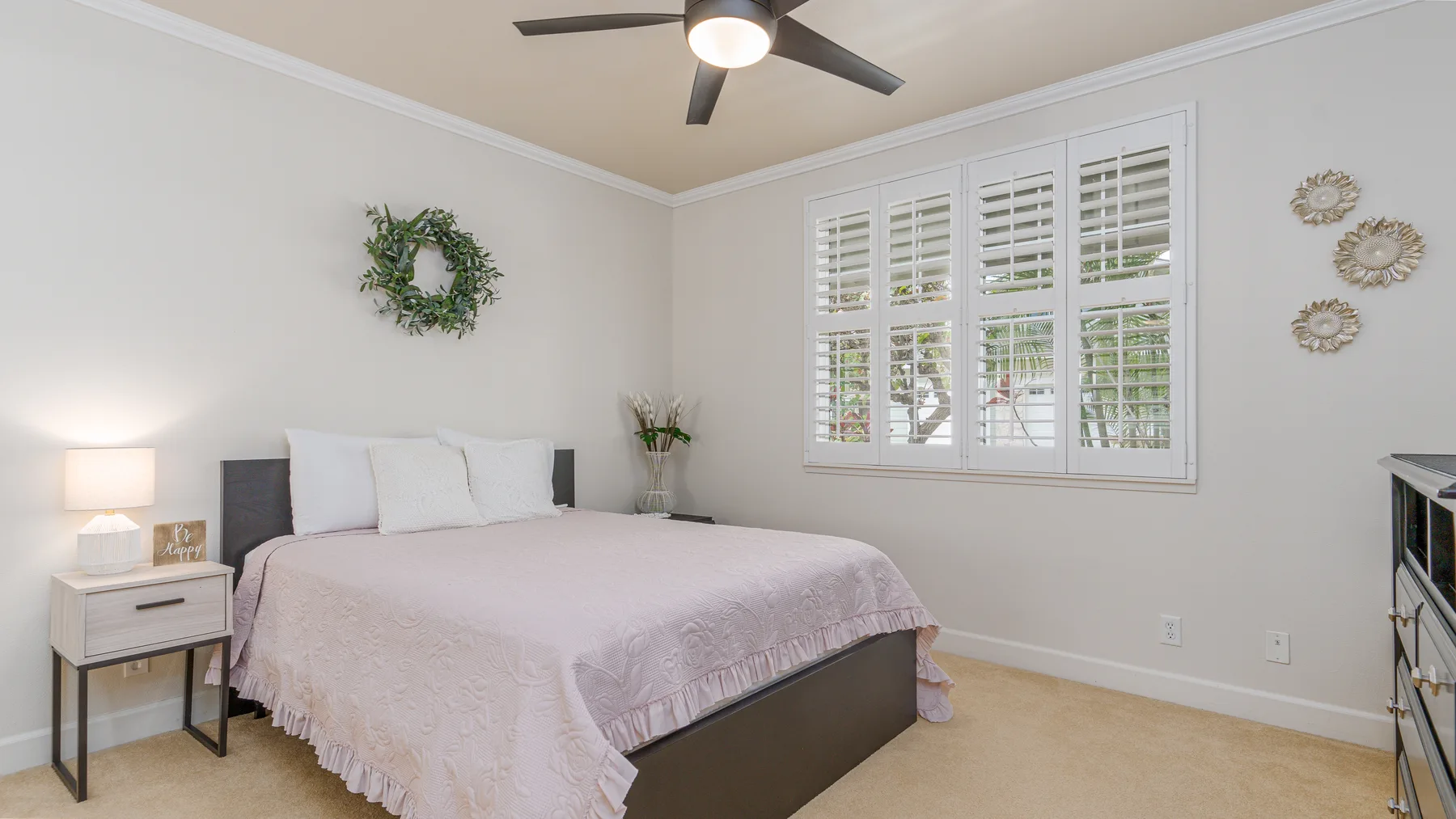 A bright bedroom with a neatly made bed beneath wide shuttered windows.