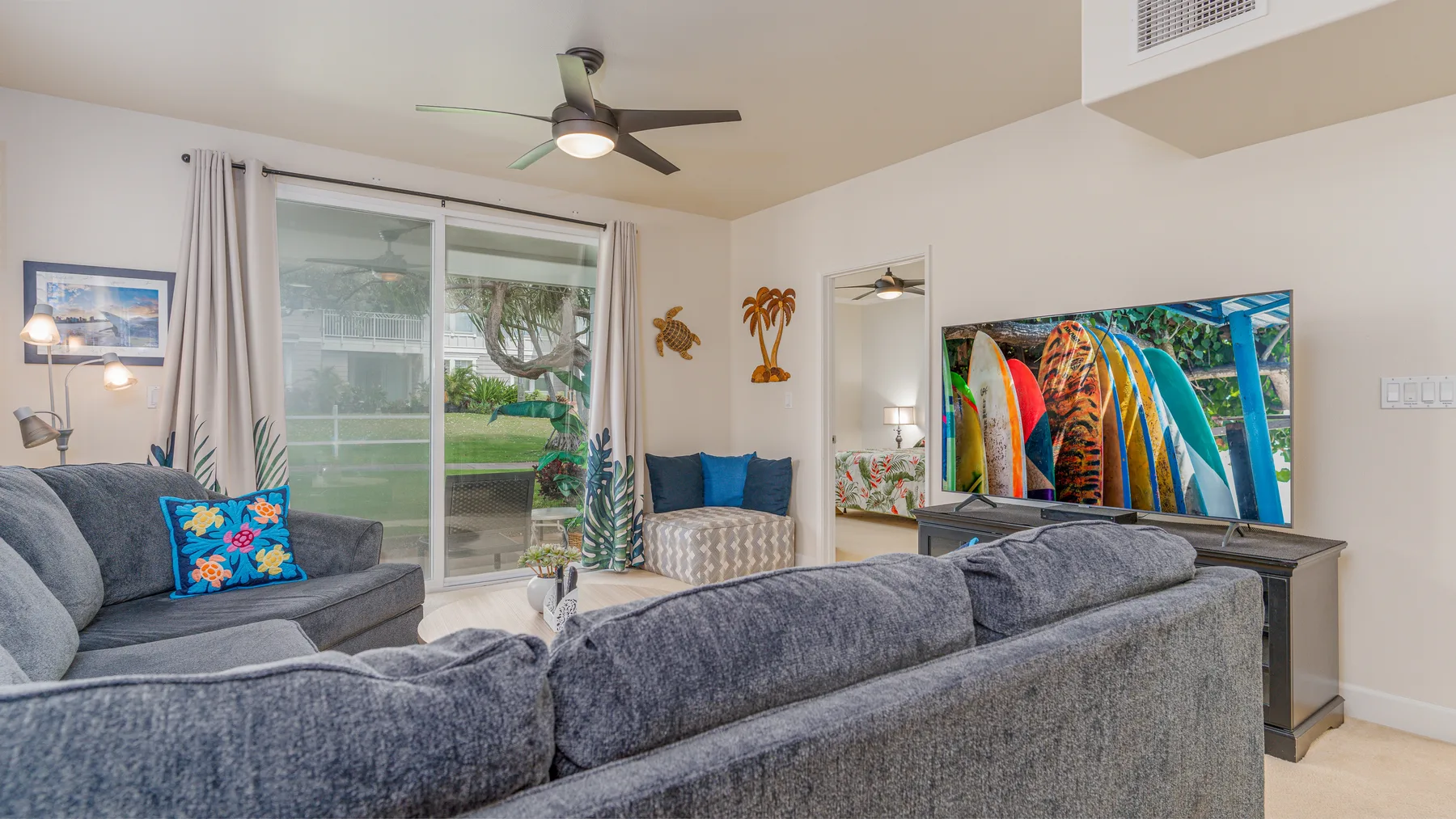 A living room with gray seating, a glass sliding door, and colorful artwork.