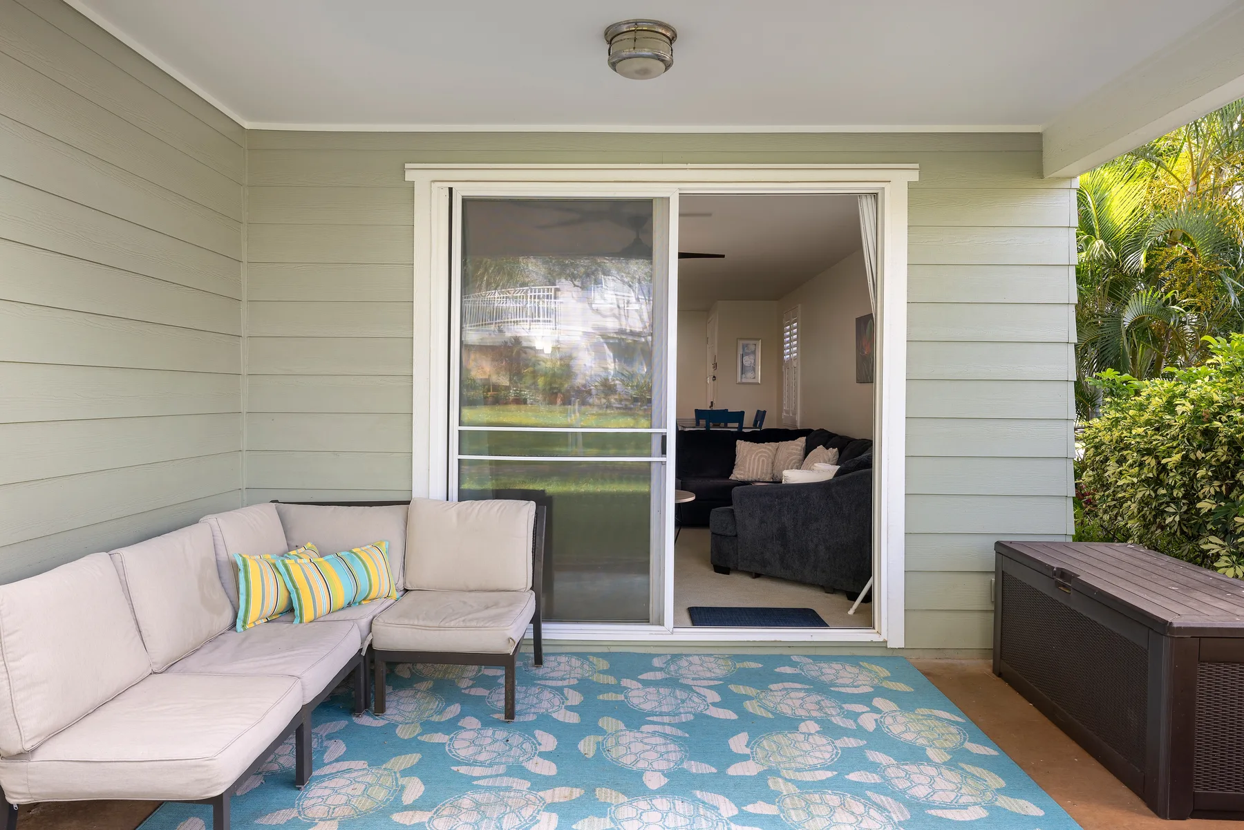 A covered patio with cushioned seating and a sliding glass door opening into a living room.