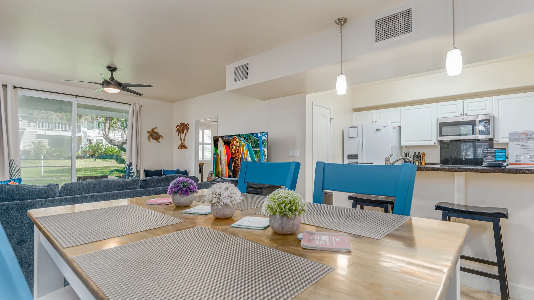 An open dining area with a long table and kitchen in the background.