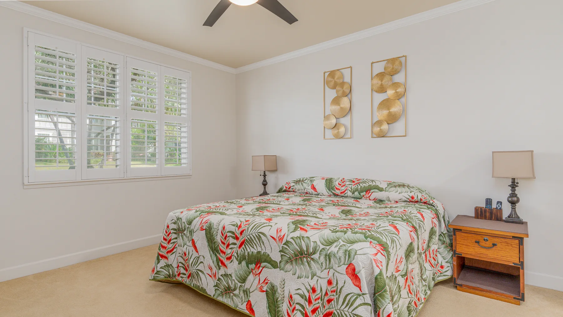 A bedroom with a floral bedspread, bedside tables, and wide windows.