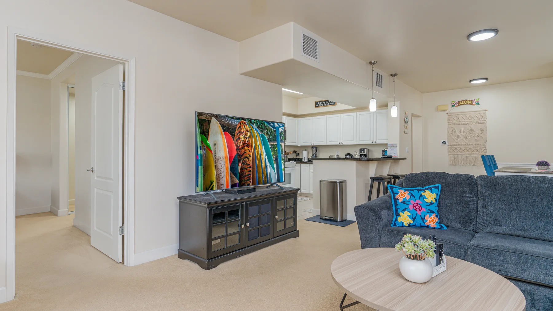 Una sala de estar con televisor y asientos azules junto a una cocina abierta.
