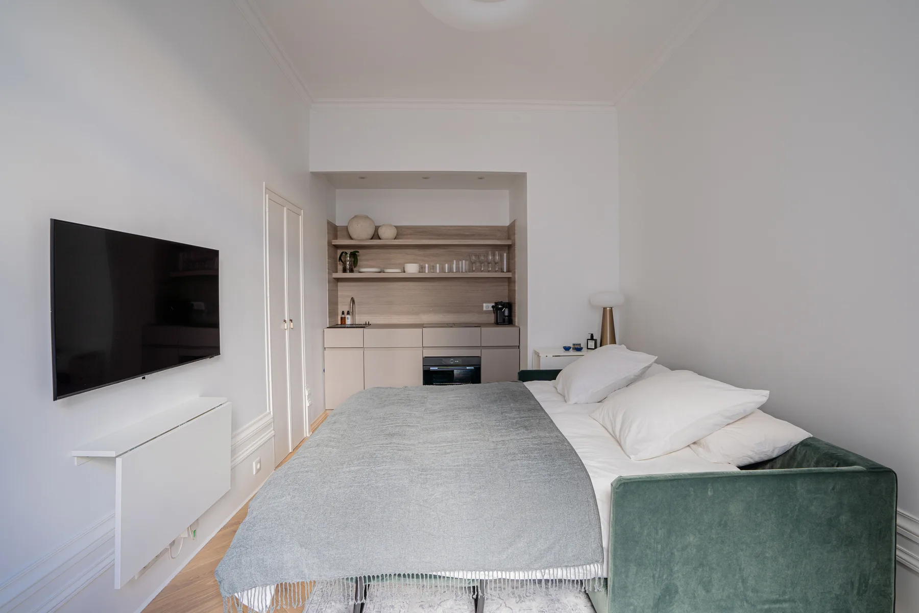 A bedroom with a bed, wall-mounted television, and kitchenette.