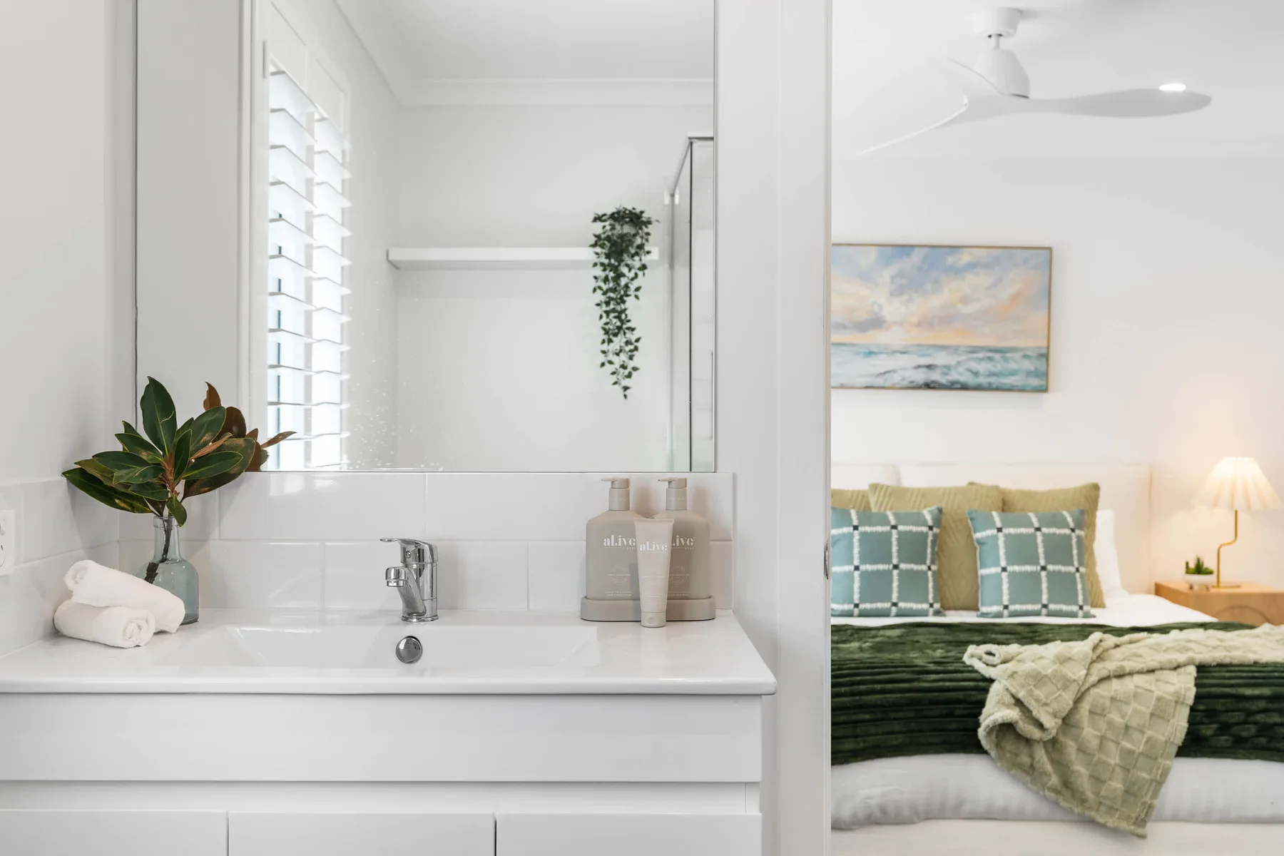 Un baño luminoso con lavabo junto a un dormitorio con la cama arreglada.