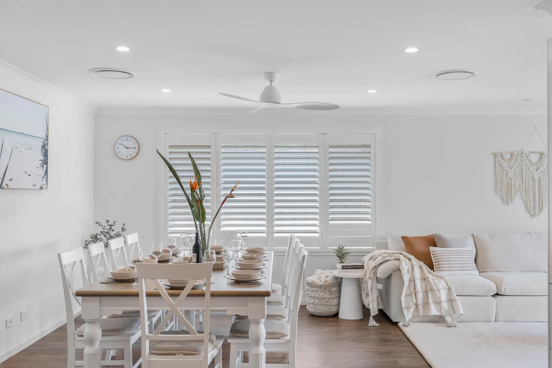 Una luminosa zona de comedor y sala de estar con la mesa puesta y asientos blancos.