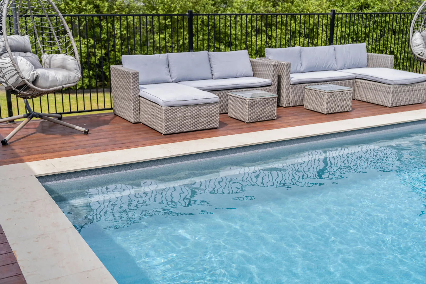 Una piscina junto a una terraza con asientos acolchados al aire libre.