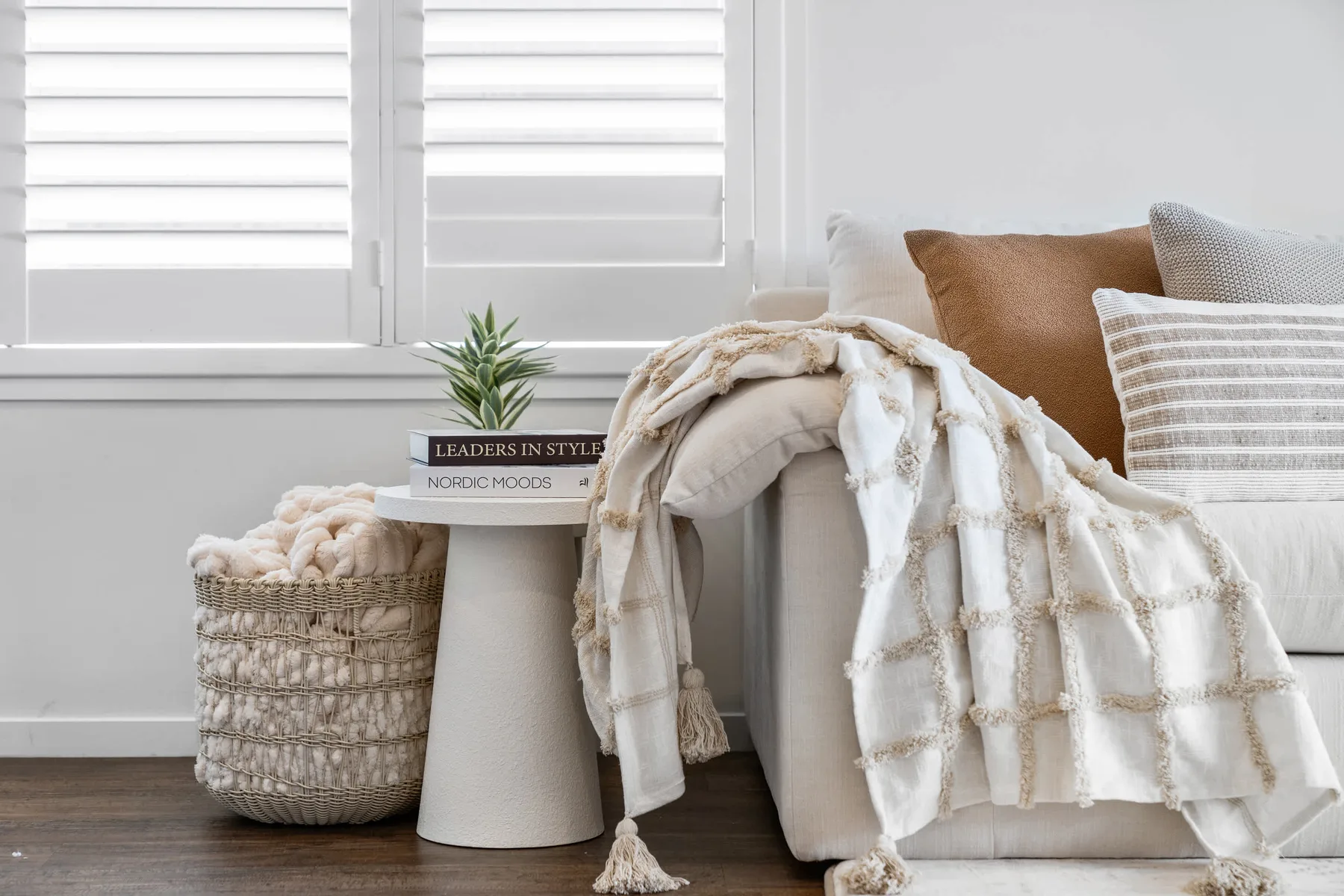 Un rincón acogedor con cojines y una manta junto a ventanas luminosas.