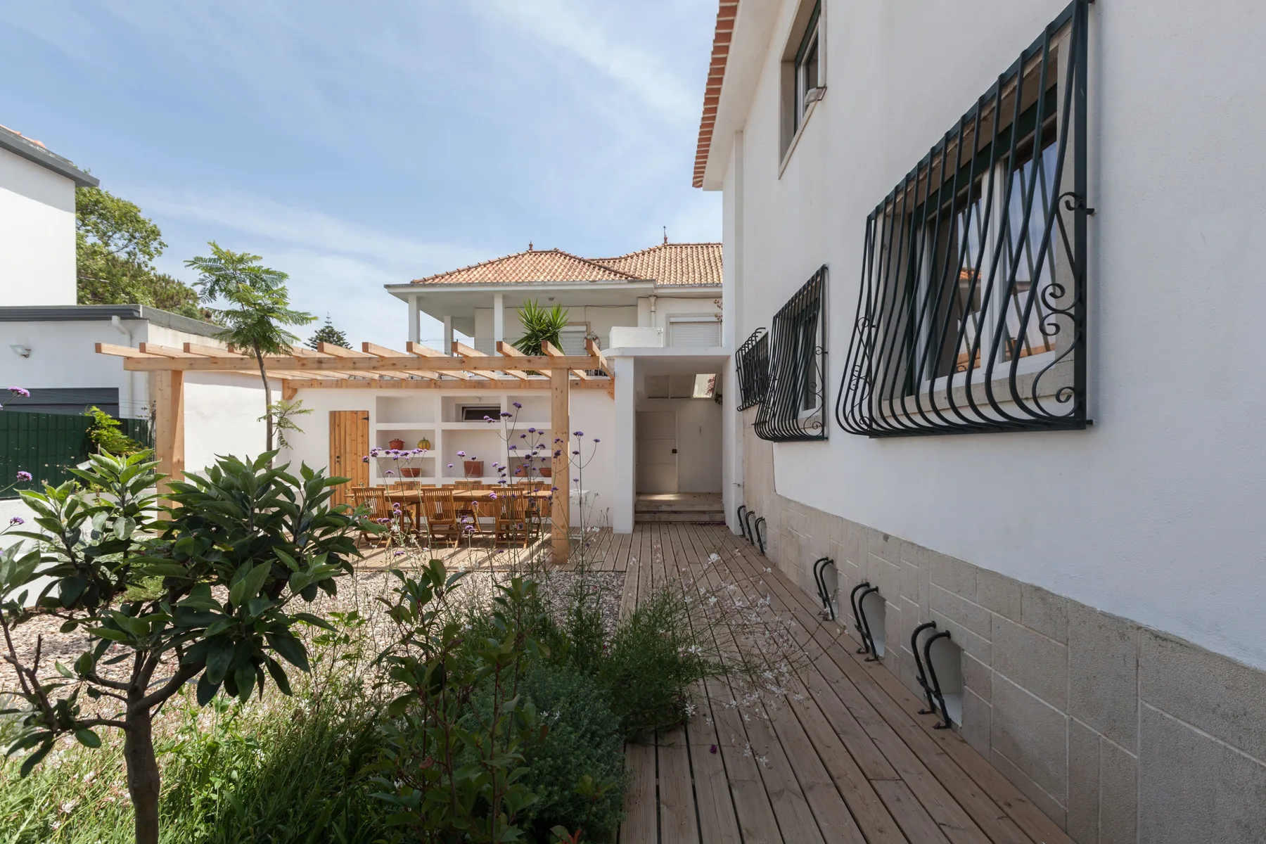Un patio pavimentado con una tarima de madera y asientos al aire libre junto a una casa blanca.